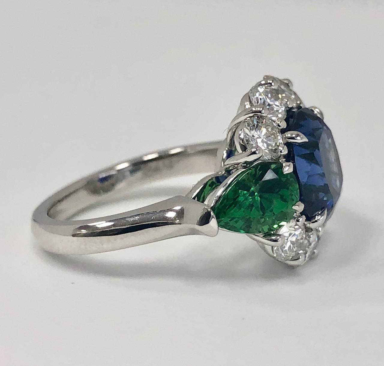 The sapphire, tsavorite and diamond cocktail ring, handmade in platinum is centered on a 4.45 carat vivid blue sapphire, accompanied by an AGL certificate. It is flanked by 2 fine Pear Mixed Cut tsavorite garnets weighing approximately 2.10 carats