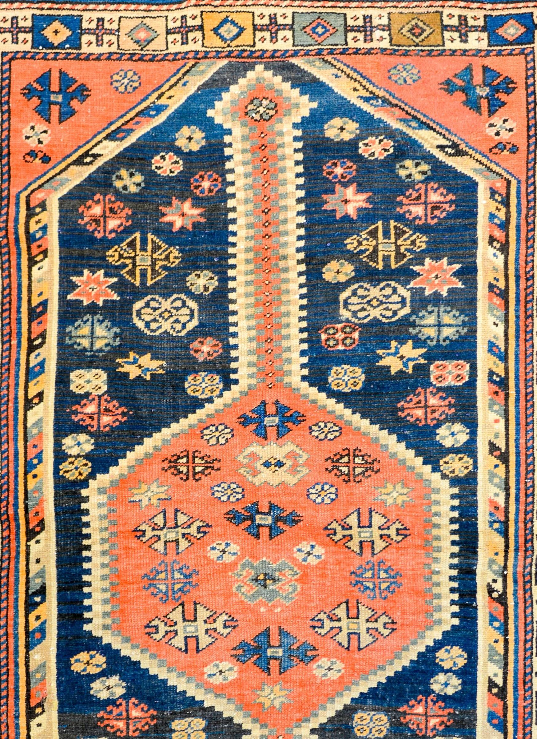 A wonderfully vivid early 20th century Persian Azeri rug with a large central hexagonal medallion woven with stylized flowers in light and dark indigo, gold, and green vegetable dyed wool, on a crimson wool background. The medallion lives amidst a