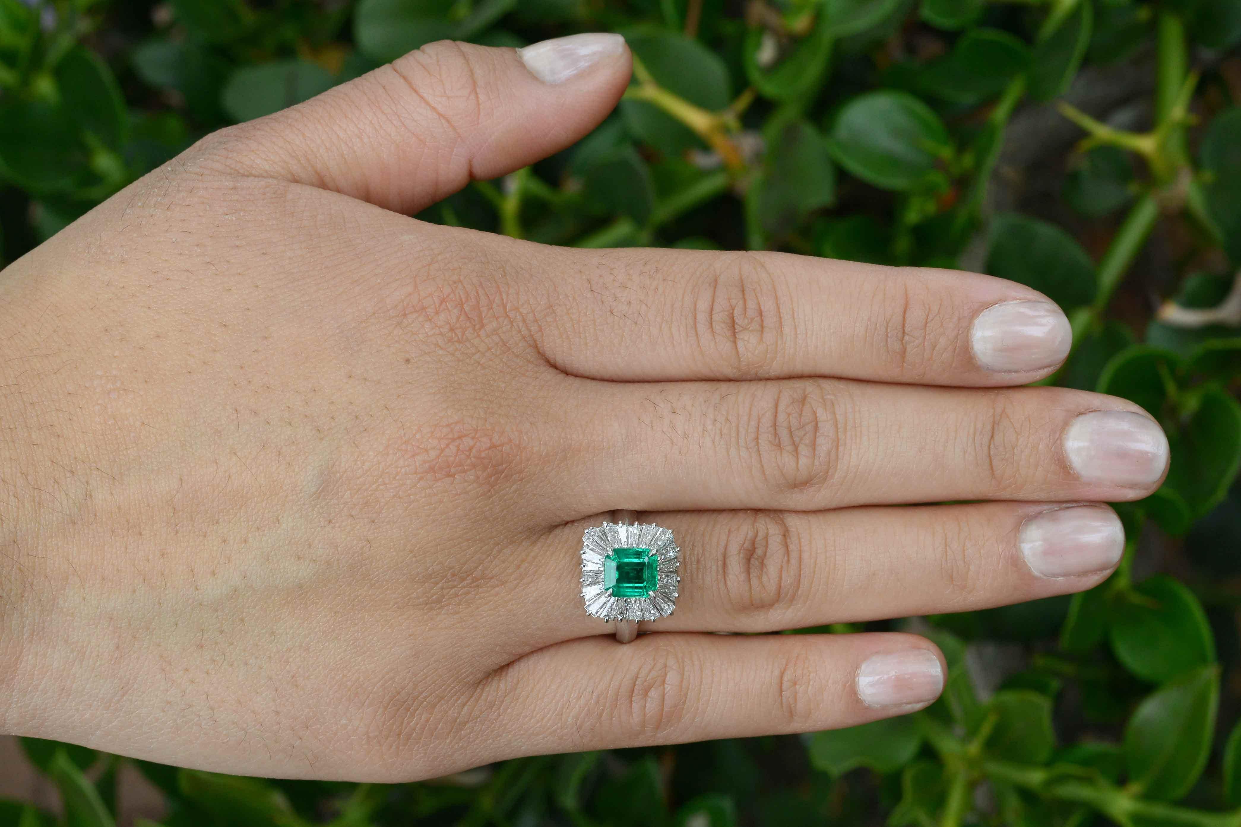 Centered by a breathtakingly lush and vivid green 1 1/2 carat emerald within a ballerina cocktail ring surrounded by 20 scintillating baguette diamonds. Named for the undulations of a tutu, the wavy design accentuates the gemstone and envelopes it