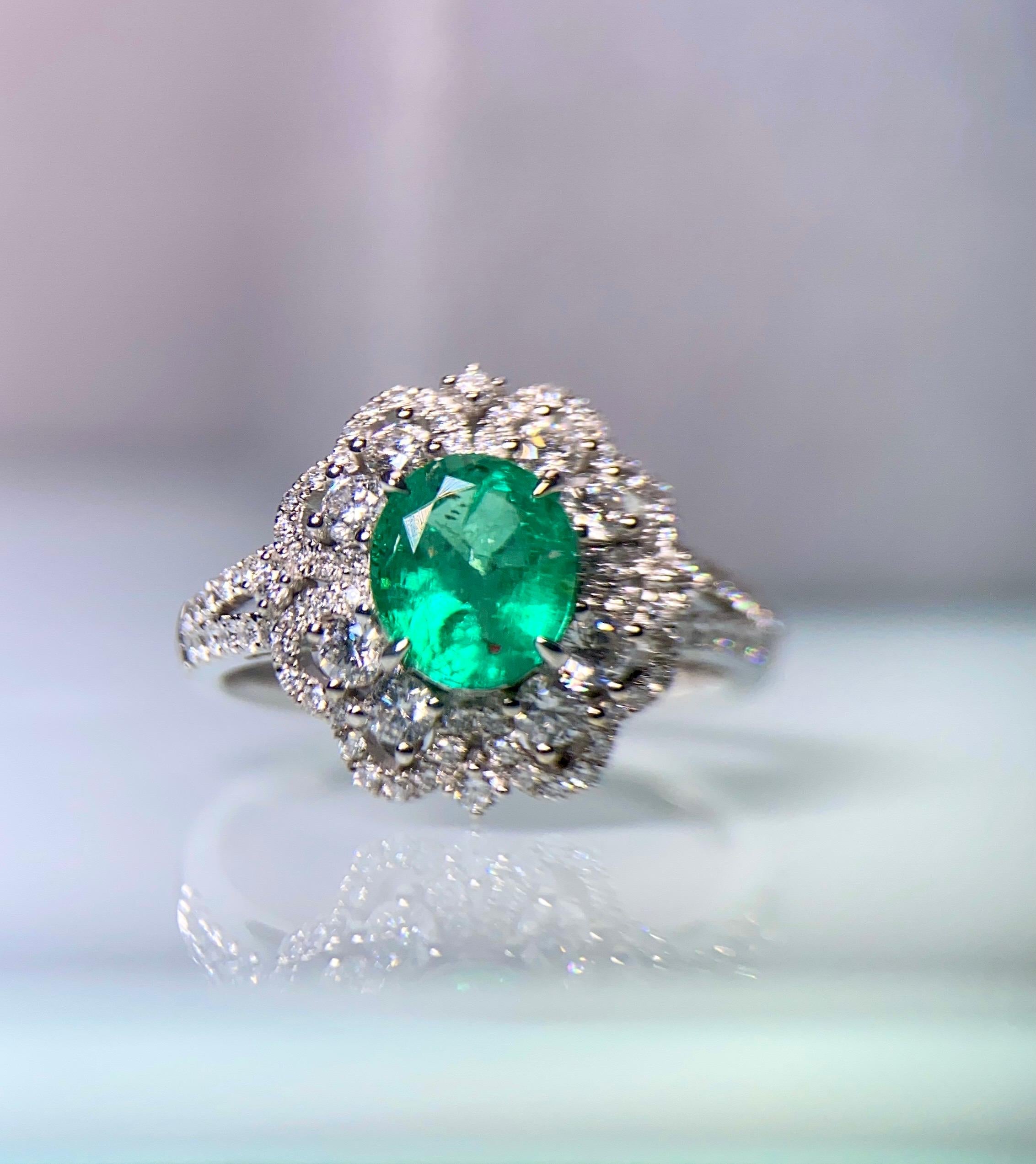 This is a flower motif clustered Emerald ring in 18K white Gold. The Emerald is surrounded by multiple diamond pave and there are 8 larger brilliant cut diamond among them. It resembles a vintage Diana setting but with more complicated details,