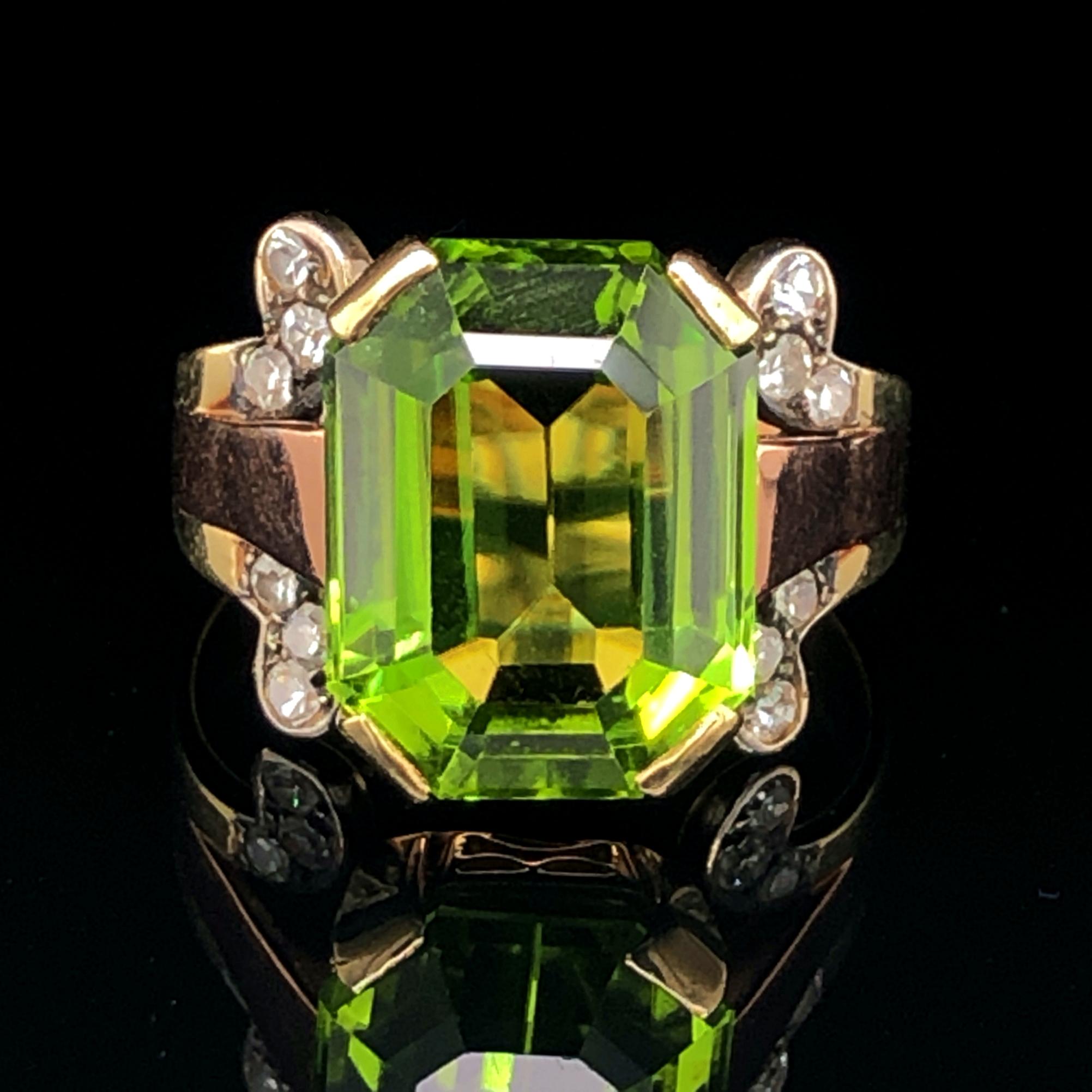 A peridot and diamond ring in 14k yellow and red gold, ca. 1950s. The emerald cut peridot weighs 11.12 carats and is a very clean gemstone with a vivid colour and crystal. The peridot is set to stand out and is neighboured by 12 single cut diamonds