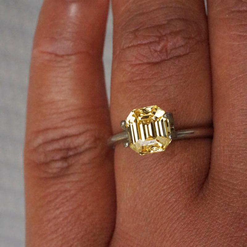 A large yellow sapphire masterfully emerald cut into just under 3 carat with gleaming facets highlighting gold which earn it a colour rating of 