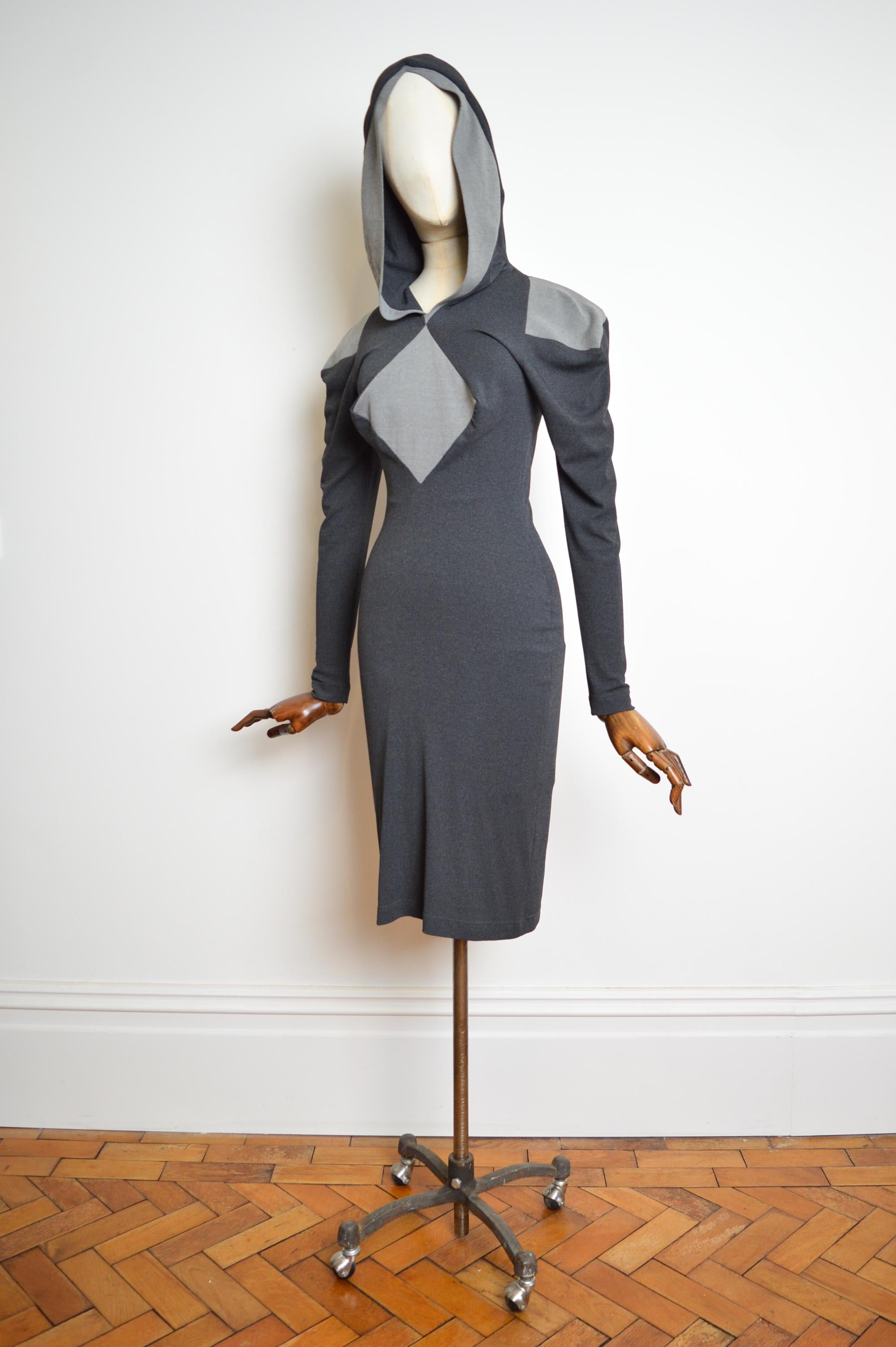 Robe à capuche rare et iconique de la Collection Sal de Vivienne Westwood pour l'automne/hiver 1999-2000. 

Cette robe en jersey gris anthracite et pierre présente une silhouette coupée en biais au niveau des genoux avec des empiècements