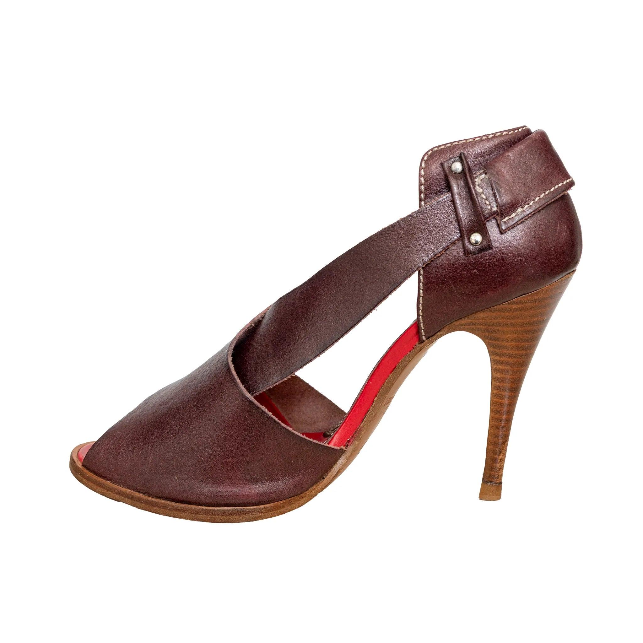 Sandali peep-toe in pelle marrone di Vivienne Westwood con gli iconici cinturini incrociati e il dettaglio della fibbia. Realizzati a mano in Italia, questi tacchi aggiungono un tocco elegante e senza tempo a qualsiasi guardaroba - perfetti per gli