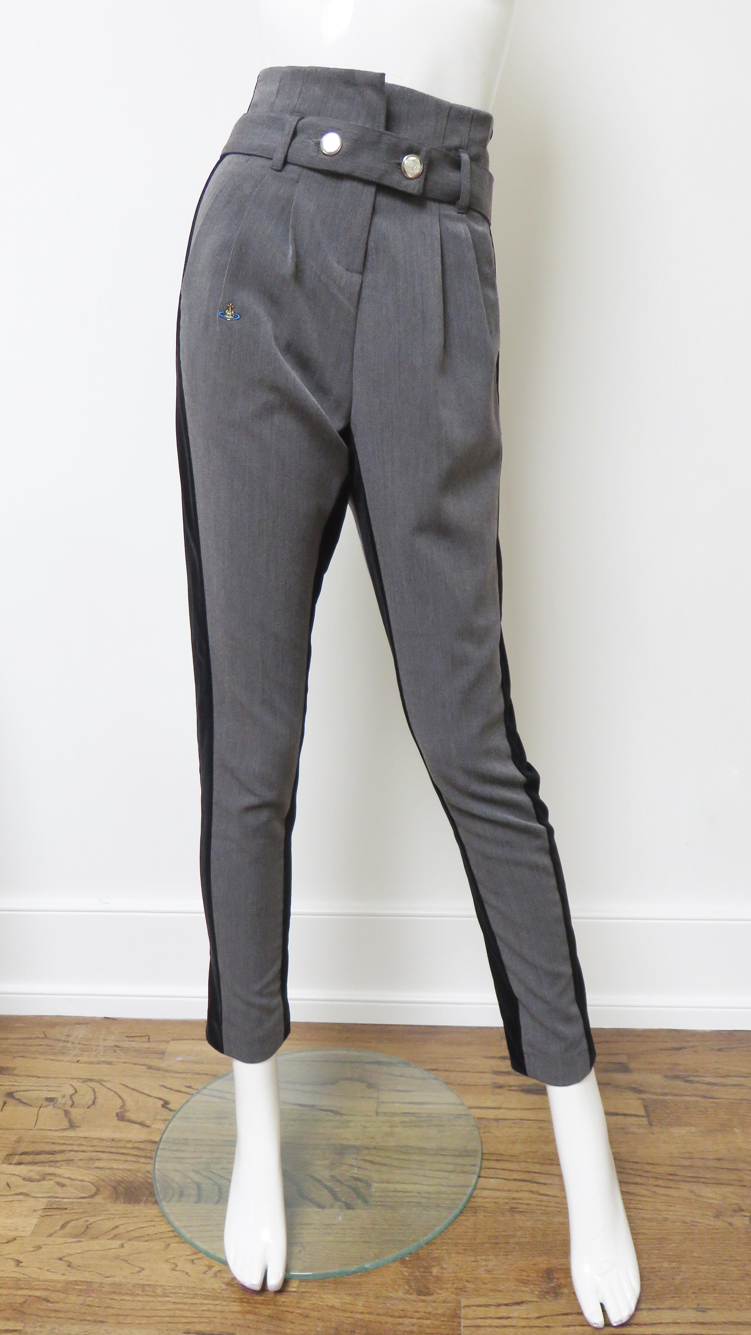 A fabulous pair of taupe grey wool and black pants by Vivienne Westwood. They are high waisted with front pleating, front pockets, a belt at the natural waistline closing with 2 silver orb inscribed signature metal buttons. The pant legs narrow to
