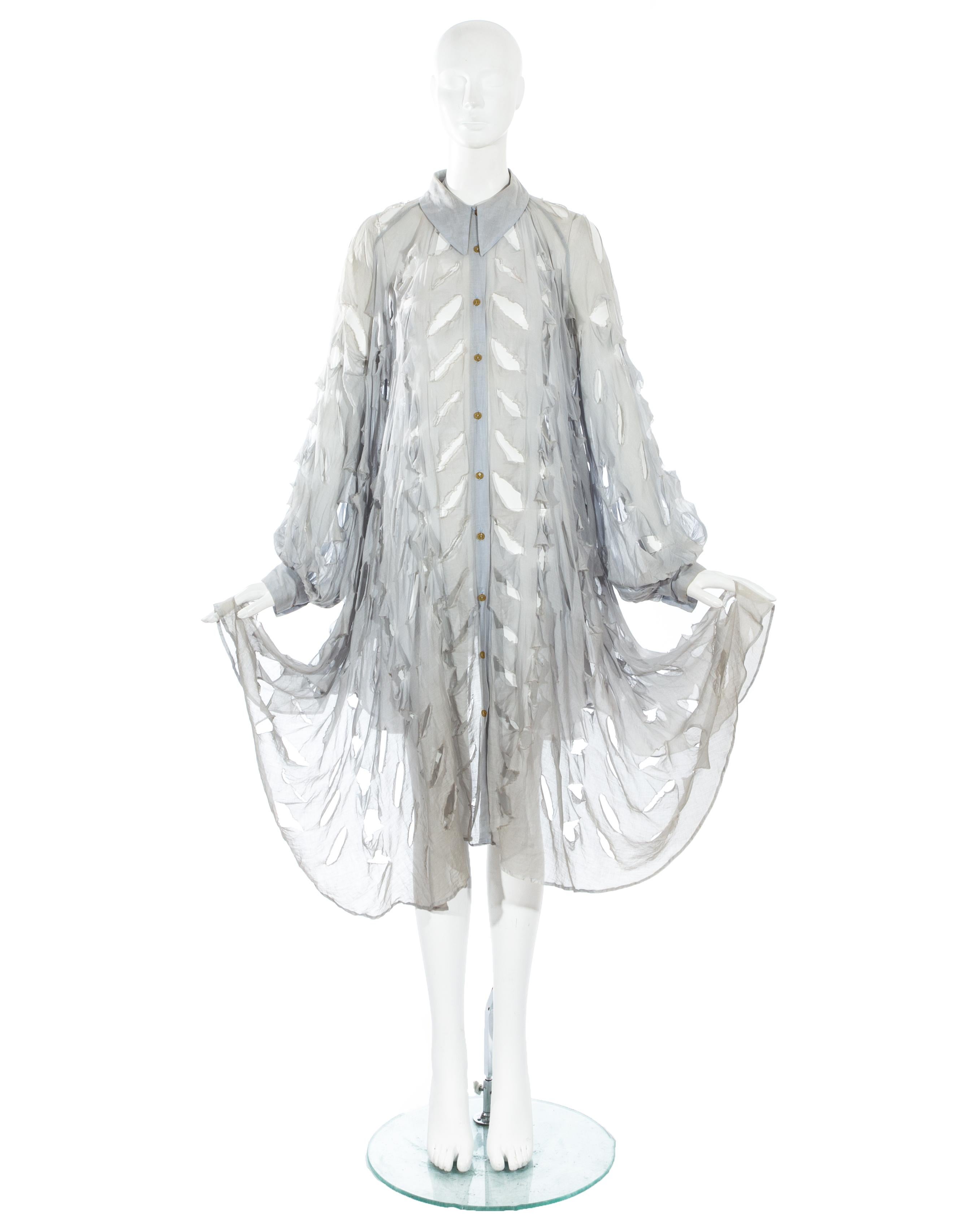 Vivienne Westwood; staubblaue Bluse aus Baumwoll-Voile in Übergröße mit weiten Läuferärmeln, spitzem Kragen und von vorne ansteigendem Saum. Signaturschlitze über die gesamte Bluse.

Cut, Slash & Pull