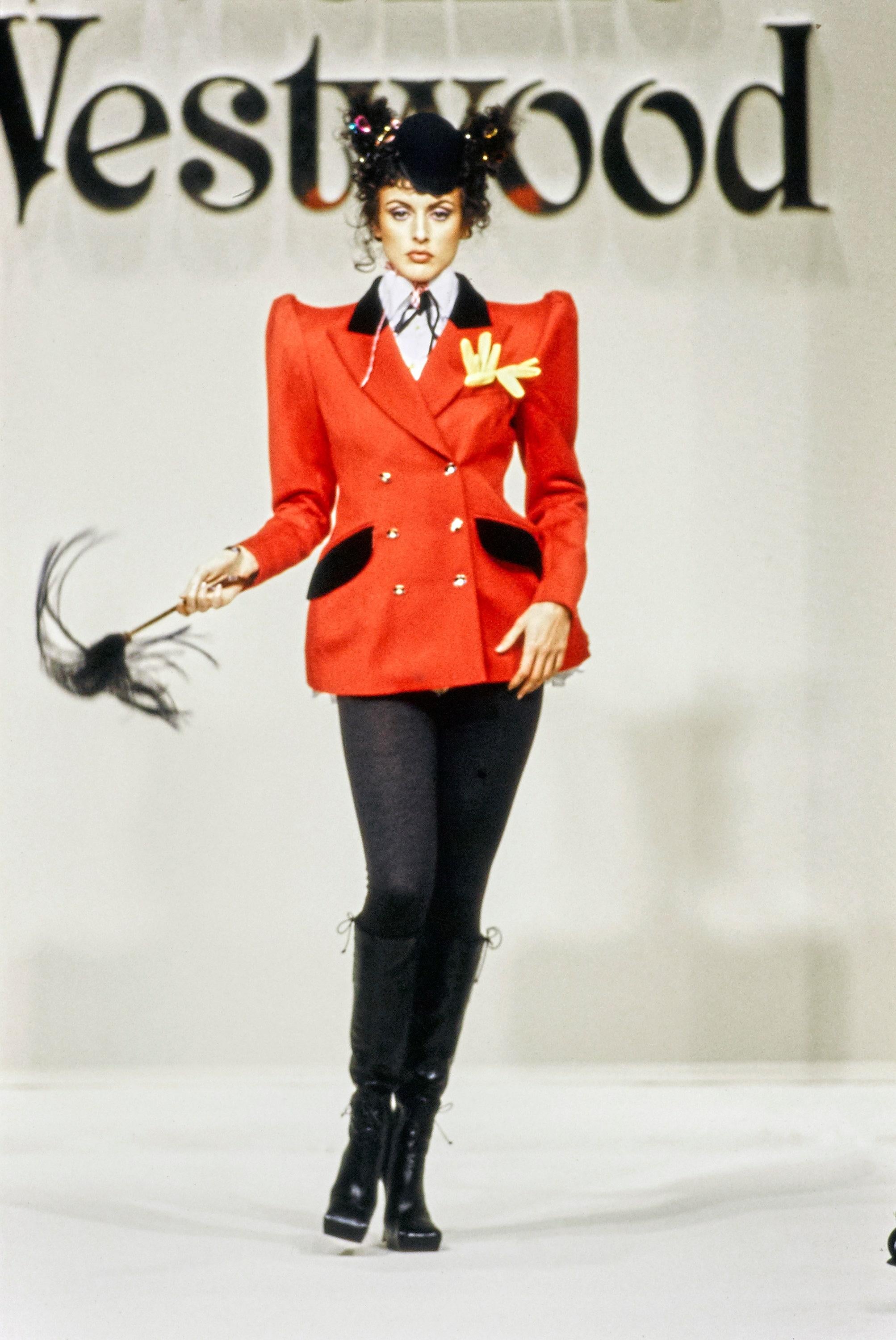 Vivienne Westwood equestrian style pant suit comprising: red wool jacket with accentuated waist, shoulder pads, large double lapel and gold orb button fastenings, high ride black velvet pants with gold ford button fastenings. 

Fall-Winter 1994