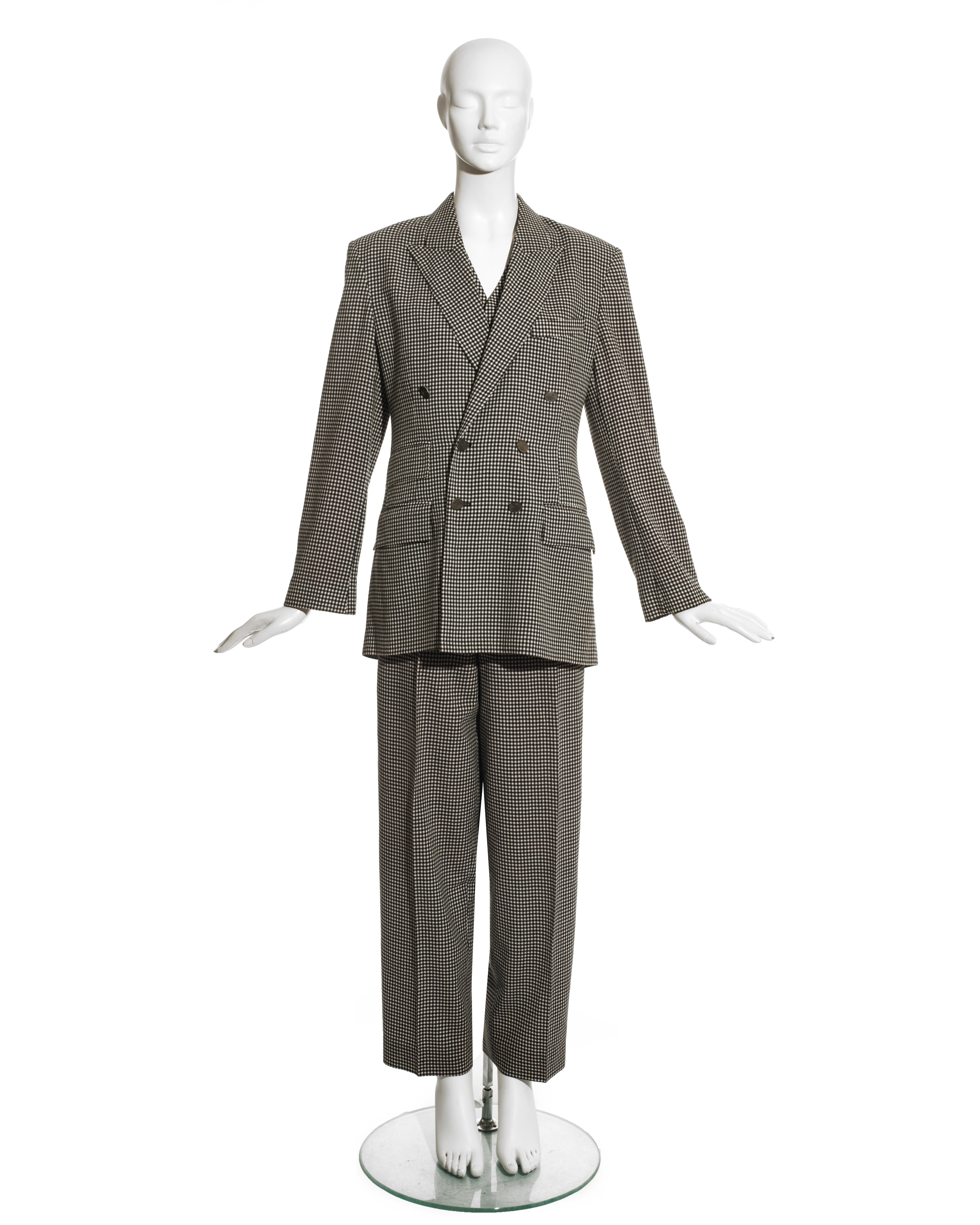 Costume pantalon unisexe en laine à carreaux noirs et blancs Vivienne Westwood comprenant : veste blazer croisée à revers, boutons orbes argentés et doublure en satin rouge, gilet croisé et pantalon carotte à taille haute. 

Automne-Hiver 1992