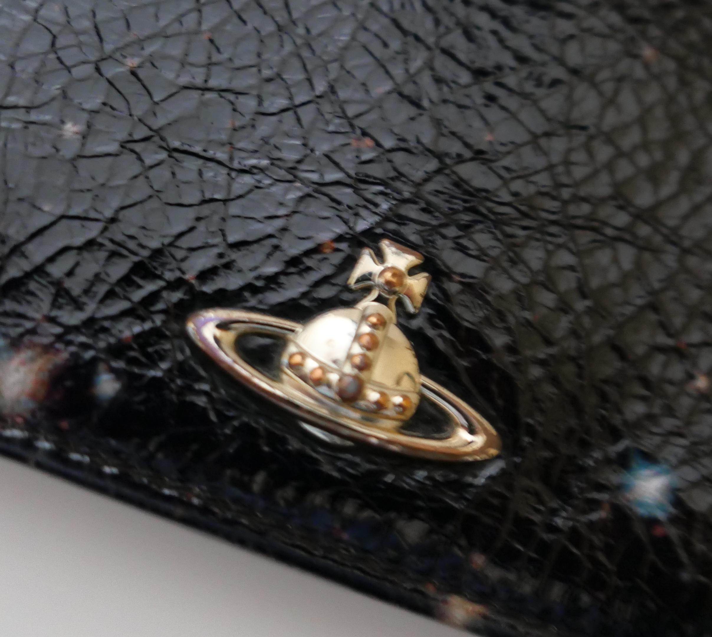 Rarísima cartera vintage con estampado de galaxias de Vivienne Westwood. Sin usar con caja. Fabricado en polipiel con textura craquelada y estampado de cielo nocturno, tiene un orbe plateado en la parte delantera, forro con logotipo y montones de