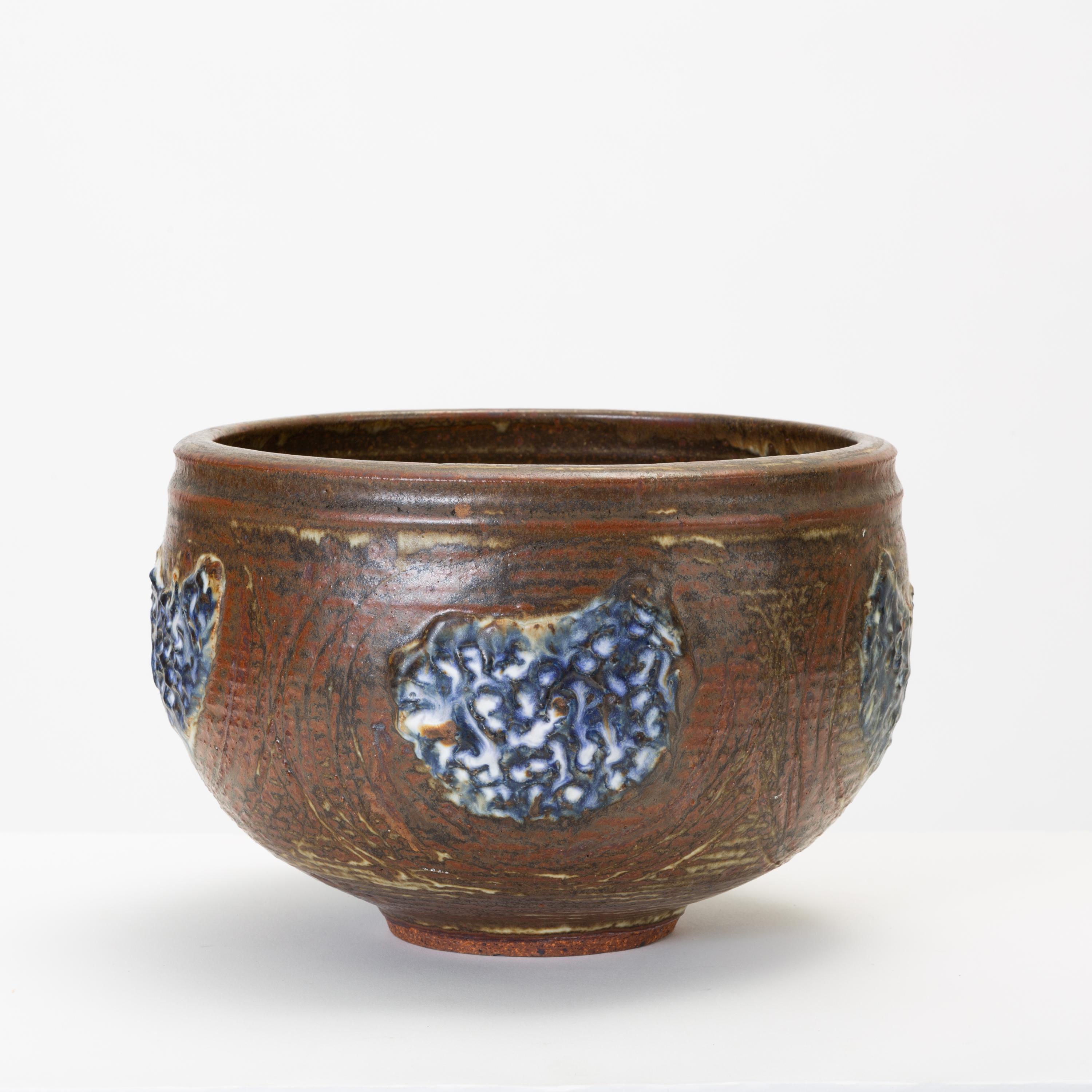 A large stoneware bowl by California-based modern ceramicists Vivika and Otto Heino is wheel-thrown with an irregular brown glaze and appliquéd decoration in a deep, royal blue. The glazed interior is gray and slightly speckled. Signed on