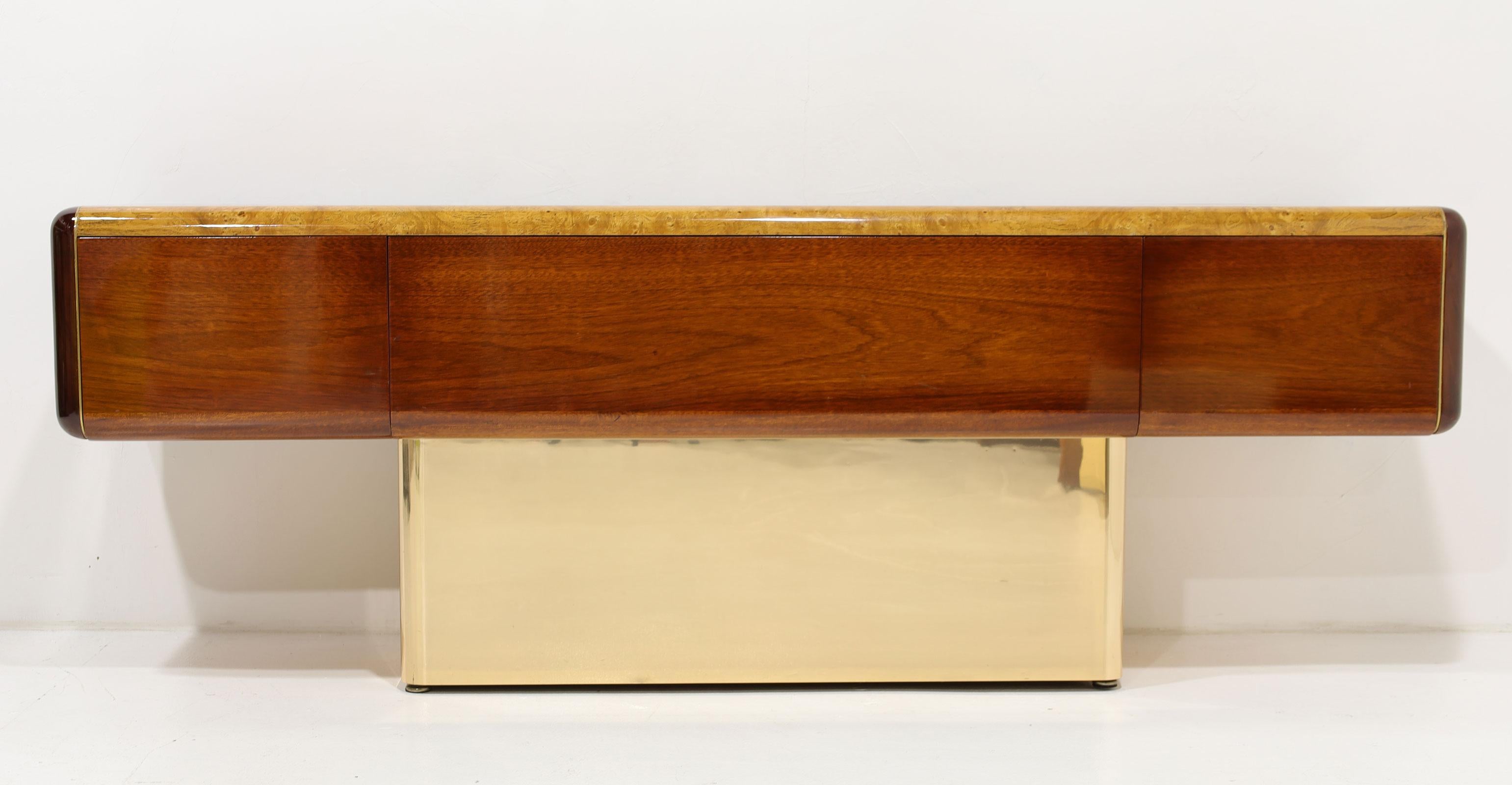 A stunning credenza by Vladimir Kagan Design Studio. Credenza floats on a wood base clad in a brass finished metal. There are three file drawers with hanging fixtures in place. Top is finished in burl wood with mahogany wood around all sides29500