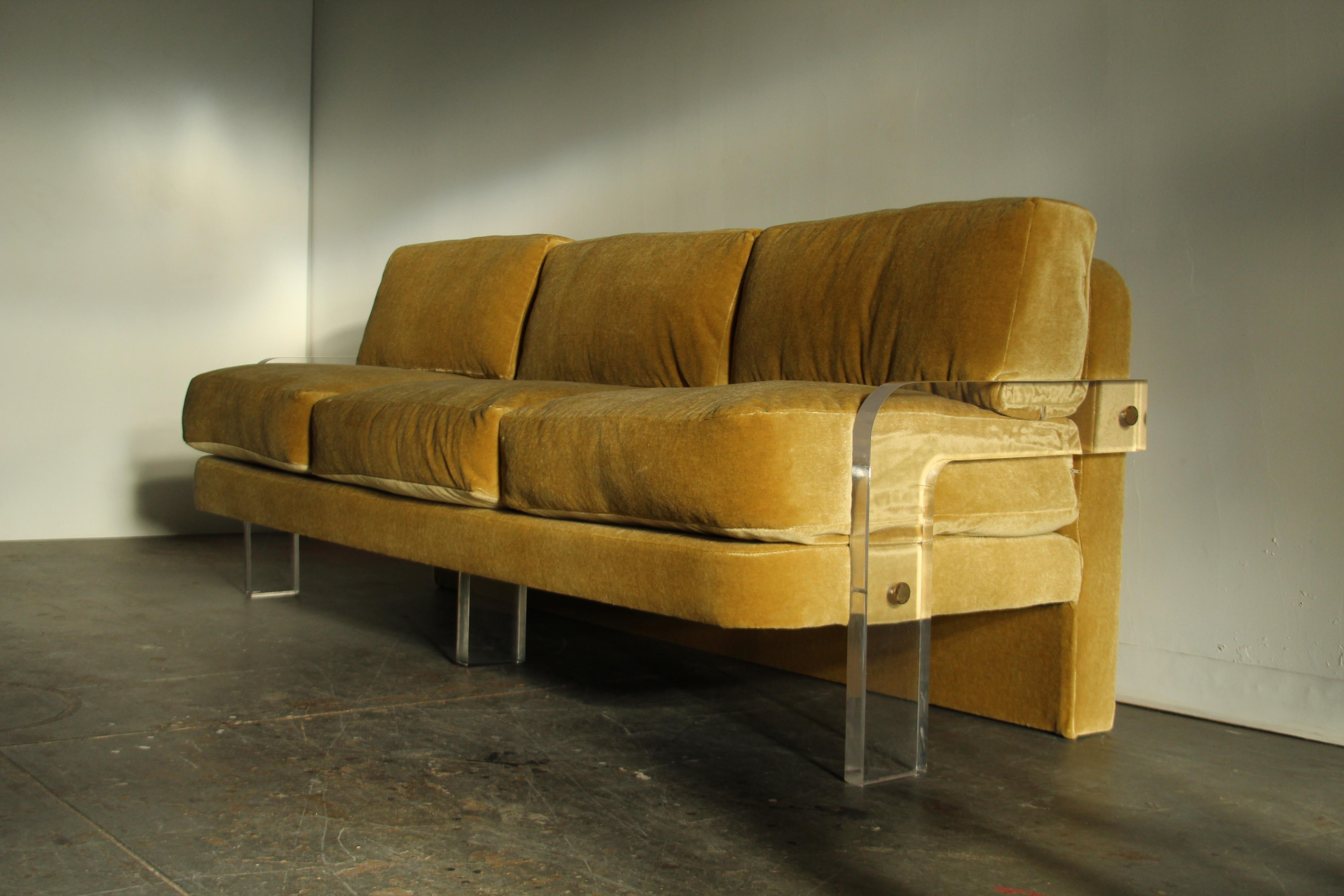 This uncommon 3-seat sofa is, quite simply, the bee's knees. Constructed of a solid wood frame with thick lucite arms and legs and brass accents, this sofa is the epitome of chic. While it remains a little bit of a mystery, this design has always