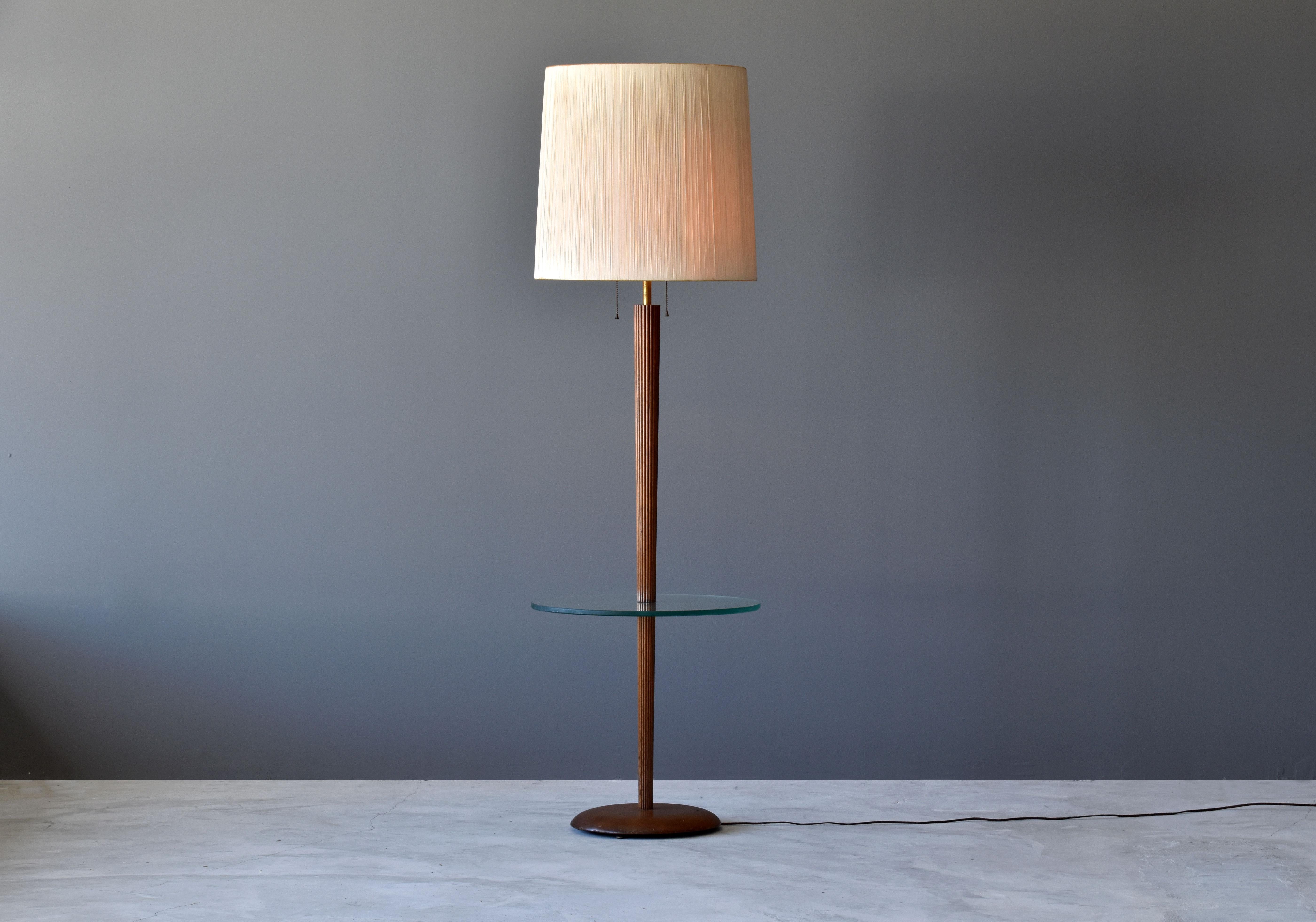 A rare and possibly unique floor lamp with a built-in side table designed by Vladimir Kagan. Produced by Kagan-Dreyfus in New York, circa 1960s. 

The rod and base are finely carved walnut and a mounted modernist glass disk serving as a side
