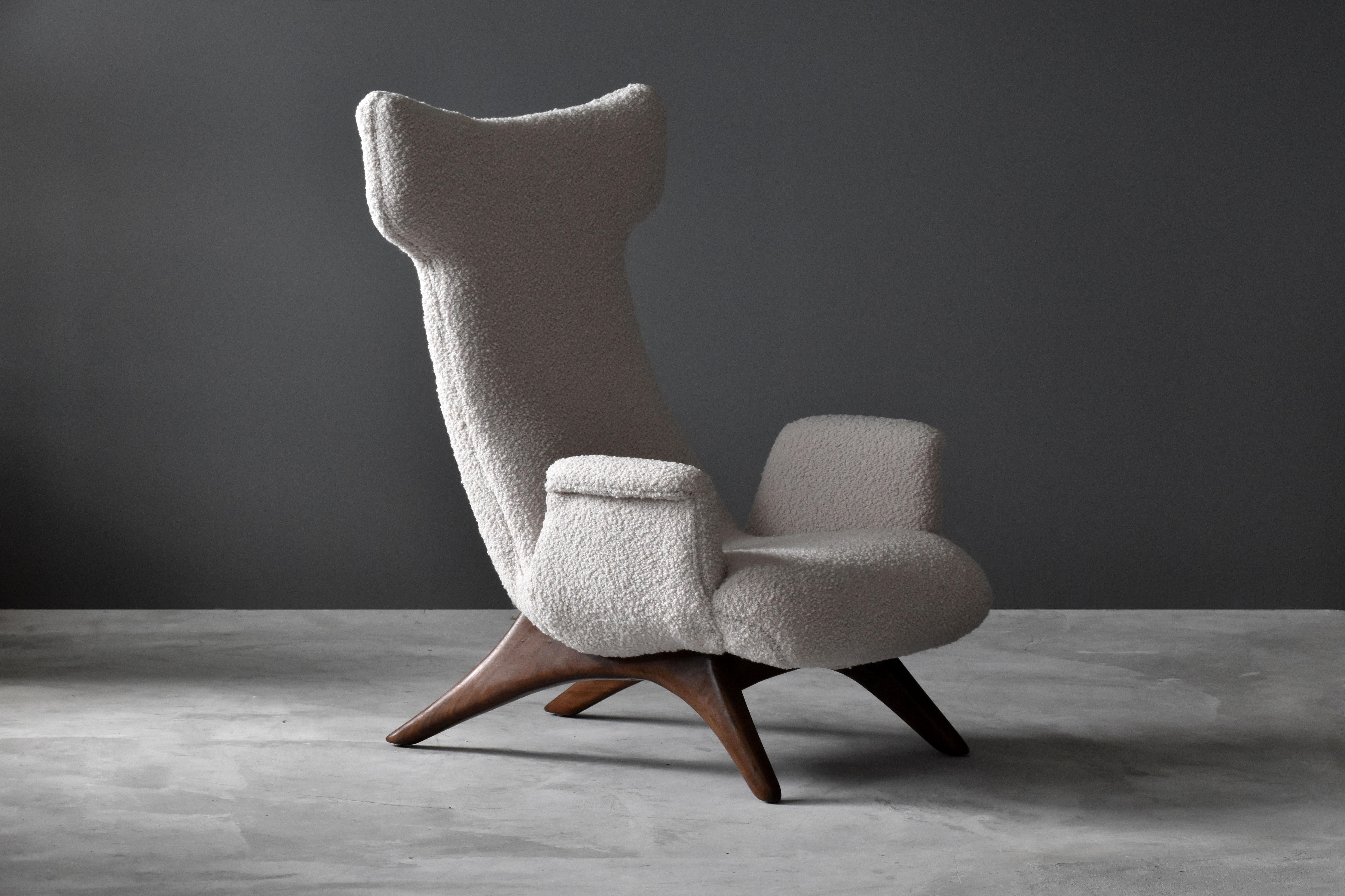 A rare wingback lounge chair, model no. 503. The soft organic forms are further enhanced by the high end bouclé fabric. Frame rests on a finely carved walnut base. Designed in the 1950s, this vintage example is produced in the 1990s, within the