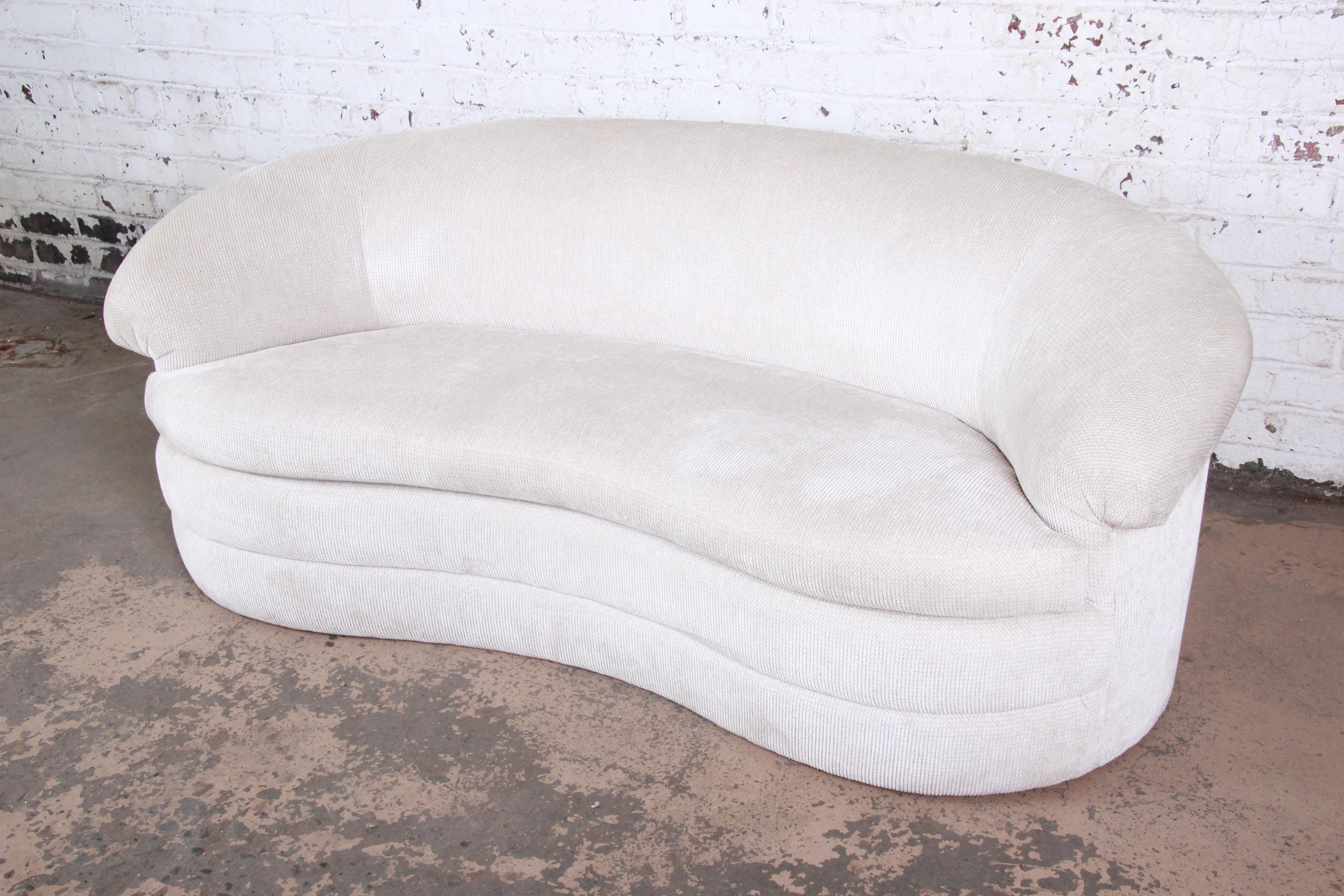 A unique kidney-shaped sofa, circa 1970s. The sofa features a nice sculptural modern design, with a curved arched back and a plinth base. The ivory upholstery is original. The sofa is in good original vintage condition, with normal minor wear