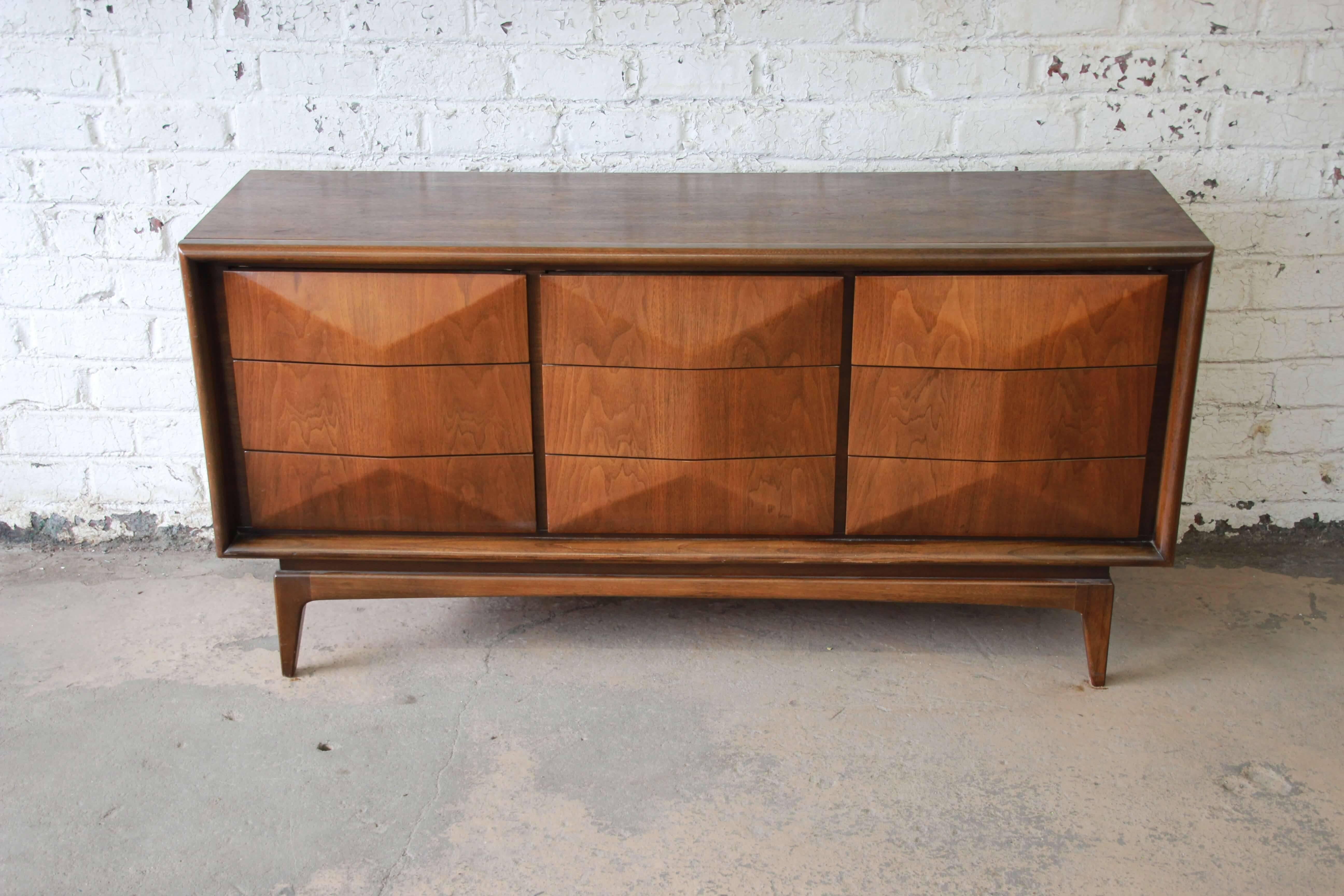 An exceptional and unique Mid-Century Modern diamond front dresser or credenza by United Furniture. The dresser features stunning walnut wood grain and a sculpted diamond front with nine hefty drawers. It is well constructed, with stylish angled
