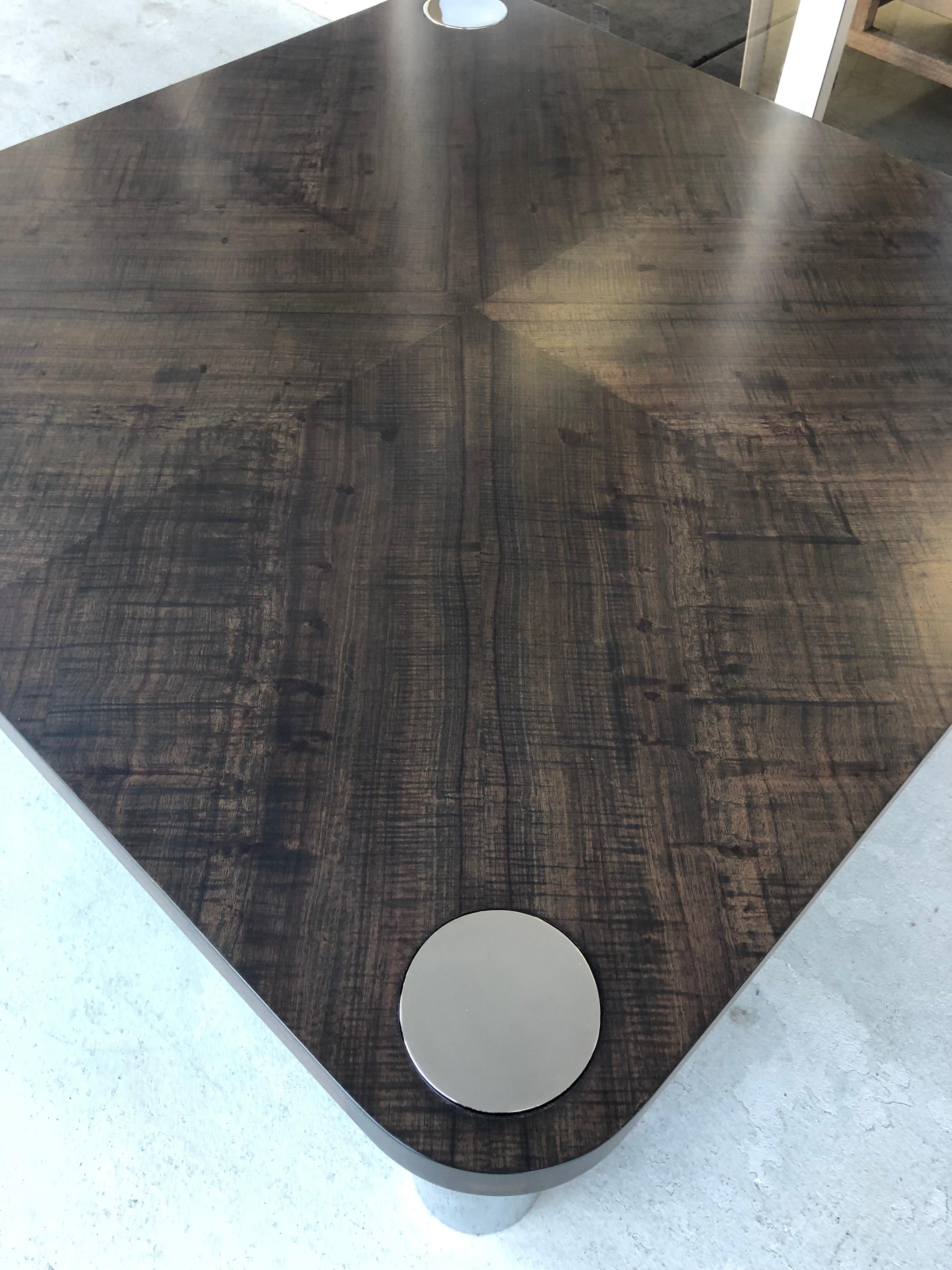 Une table en bois avec de gros pieds en acier inoxydable poli miroir. Le dessus présente un motif de grain subtil mais magnifique. Finition en ébène clair.
