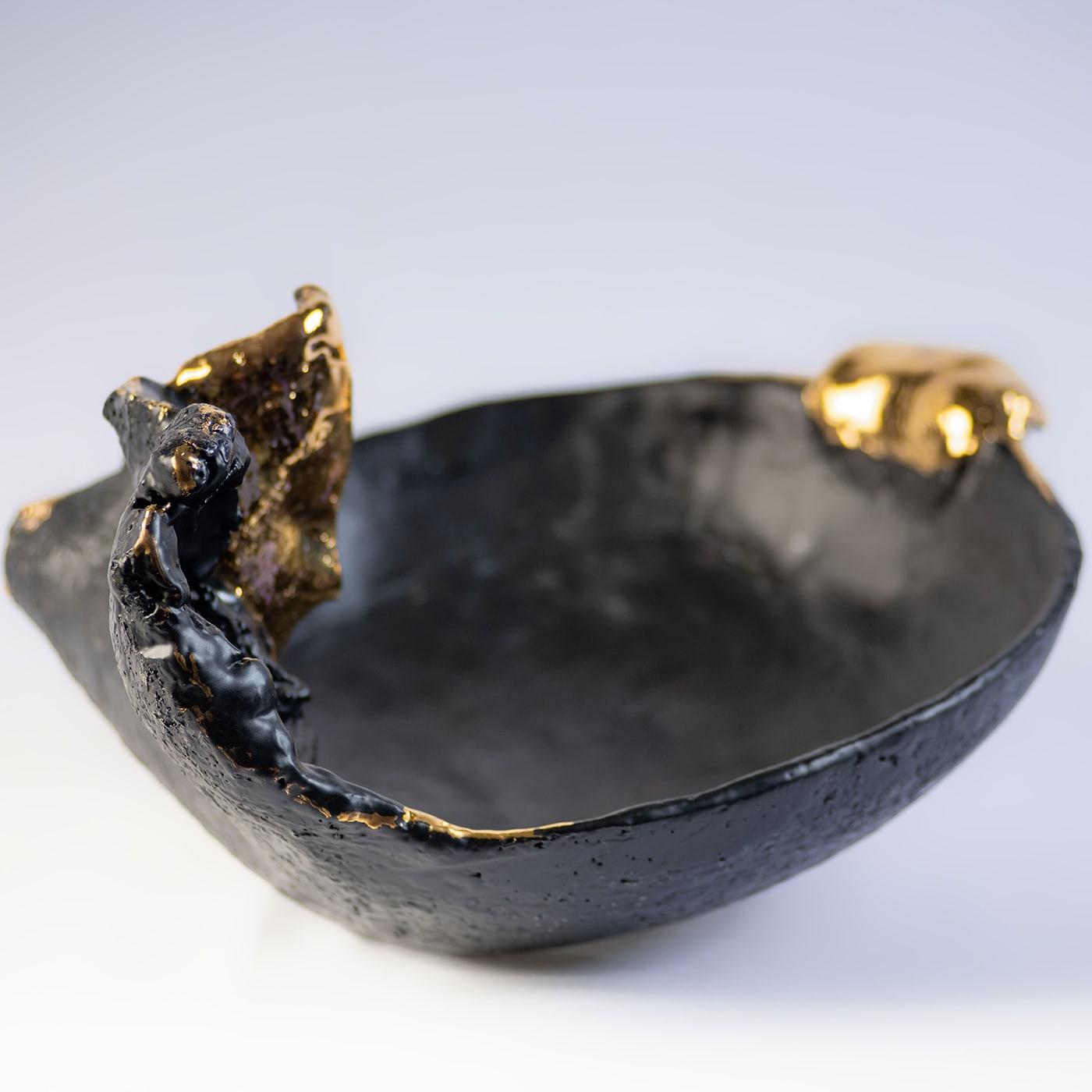 A figure seemingly trying to detach from darkness to reach the light is the outstanding trait lending this centerpiece bowl its poetic allure. Glazed in matte-black, it is luxuriously accented with polished gold inserts that emphasize the