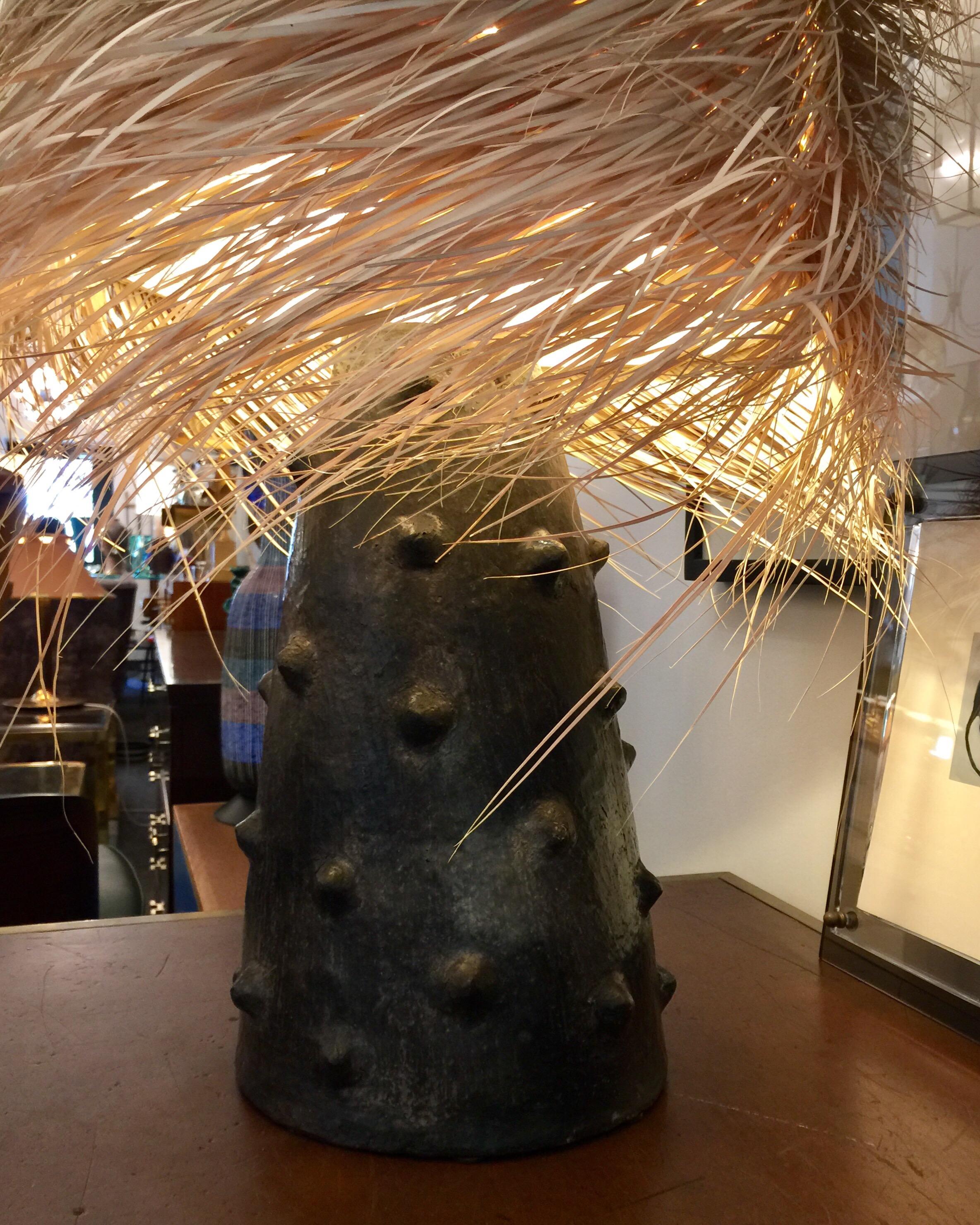 This large volcanic ash finish on terracotta lamp base with dimples throughout, is topped by a custom made palm fringe lamp shade. 

Note: Diameter of terracotta base only is 10.5 inches and 17 inches tall.