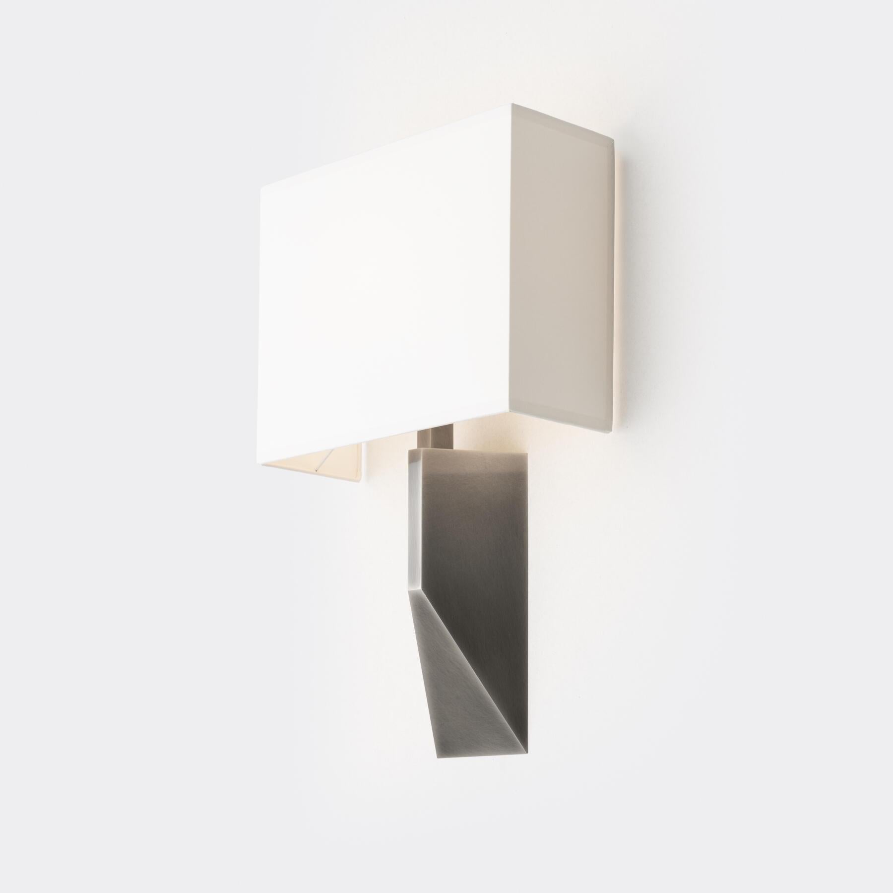 Our Volume Sconce is a statuesque design with a substantial architectural base that appears as a revised pyramid when viewed in profile. It is topped by a three-sided aquarelle shade, allowing for tight mounting to a wall.
