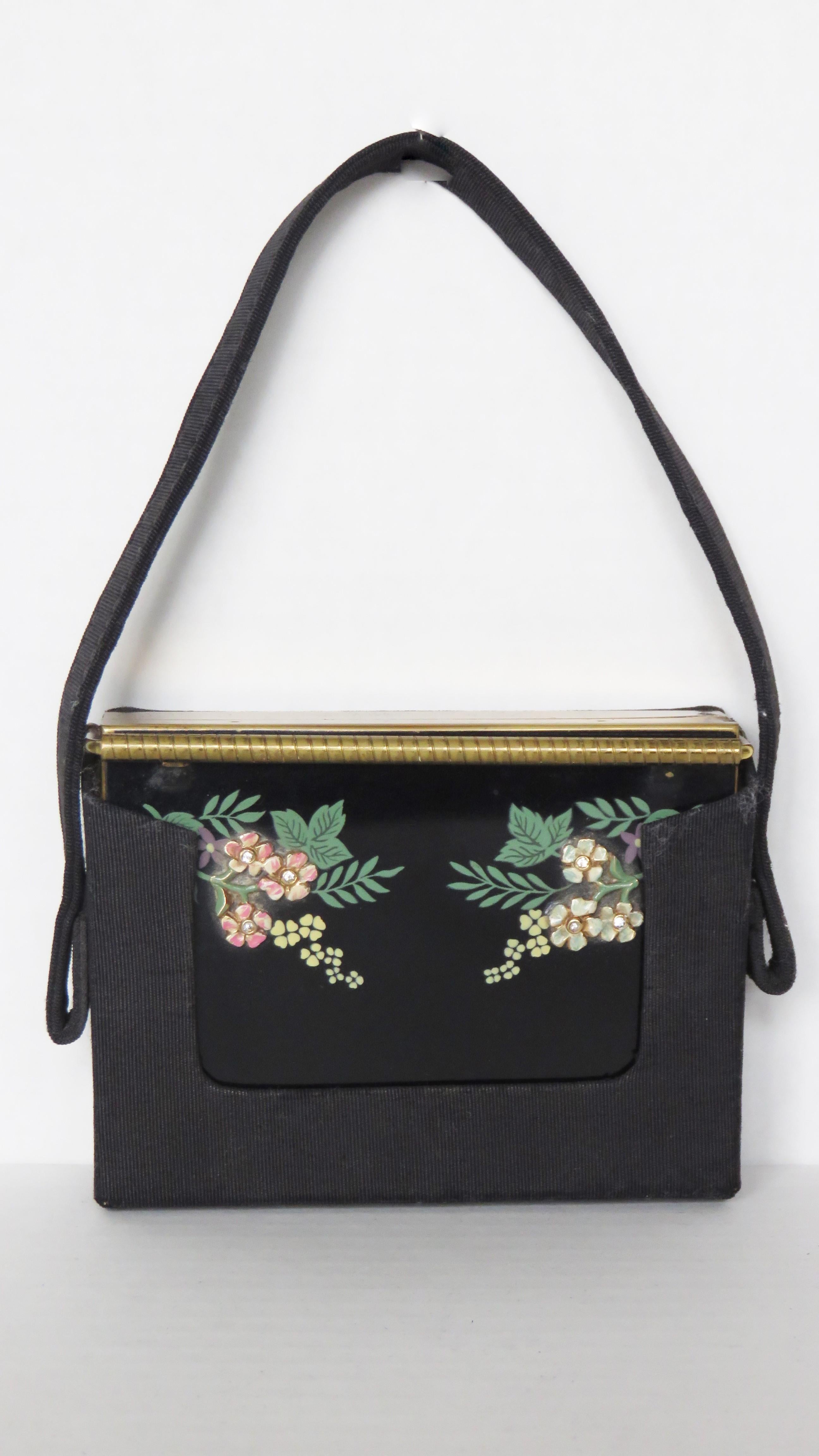 A gorgeous black enamel compact, minaudiere, purse from Volupte.  It has a black front decorated with enamel flowers and painted leaves on either side and the back is brushed gold metal.  It closes with a fine bar that closes over the top and it