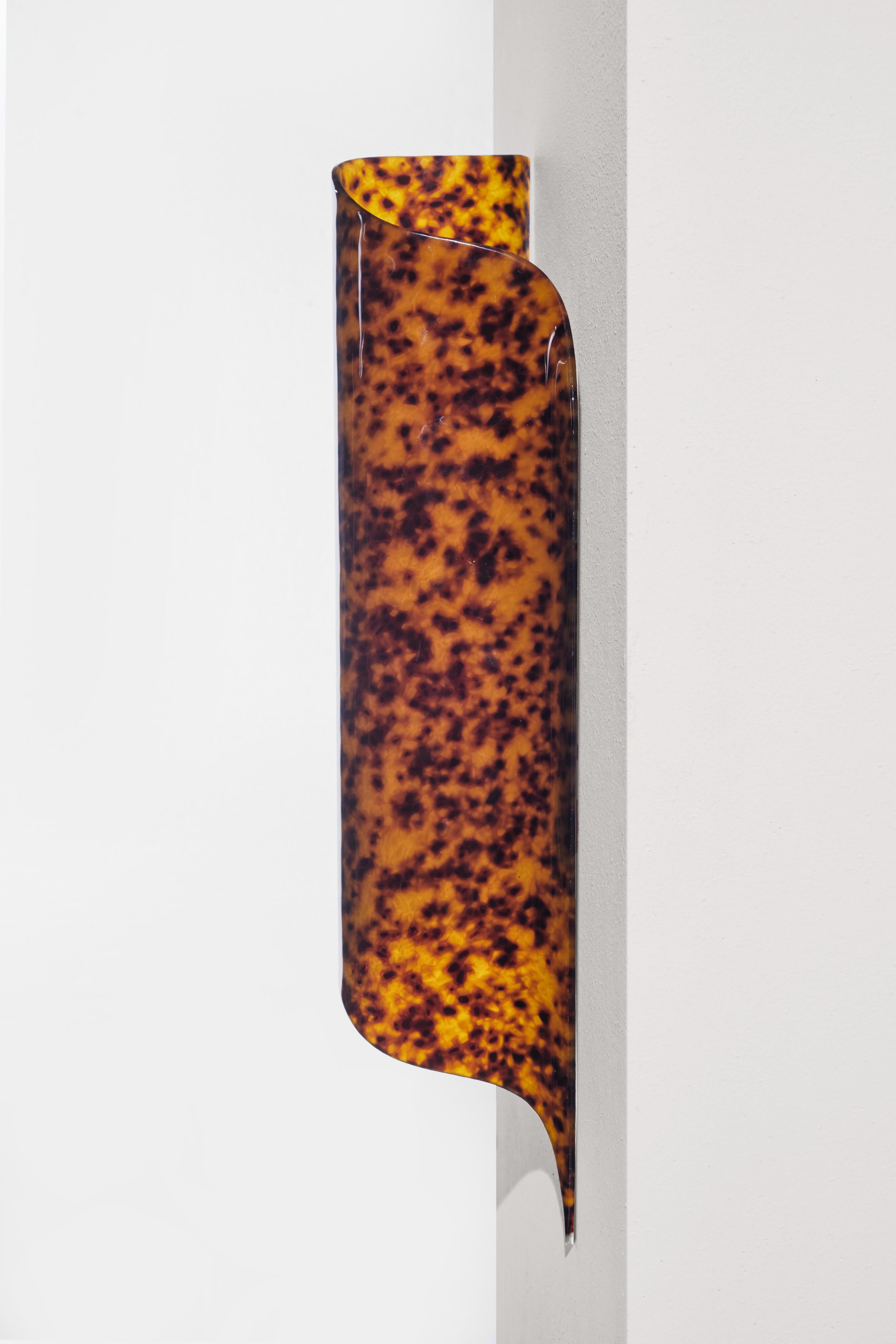 Die VOODOO Wandleuchte besitzt eine glatte, transluzente, schildpattähnliche Oberfläche aus gegossenem Acryl, die in ihrer Schönheit mit Edelsteinen vergleichbar ist. In den 1950er Jahren ein begehrtes Modematerial, erlebt die Ästhetik von