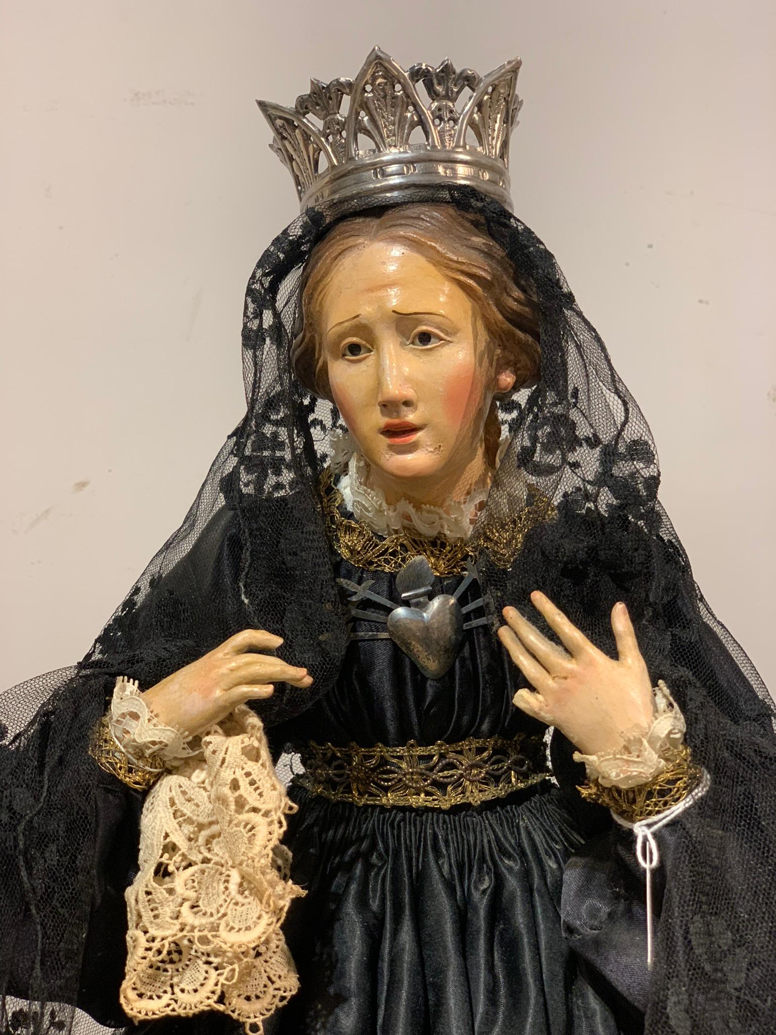 Sculpture depicting Madonna in black silk dress with lace headdress. The figure is in wood covered by fabric clothes, the head and hands are in polychrome terracotta.
The sculpture is completed by a silver heart-shaped crown and tiara on the chest.