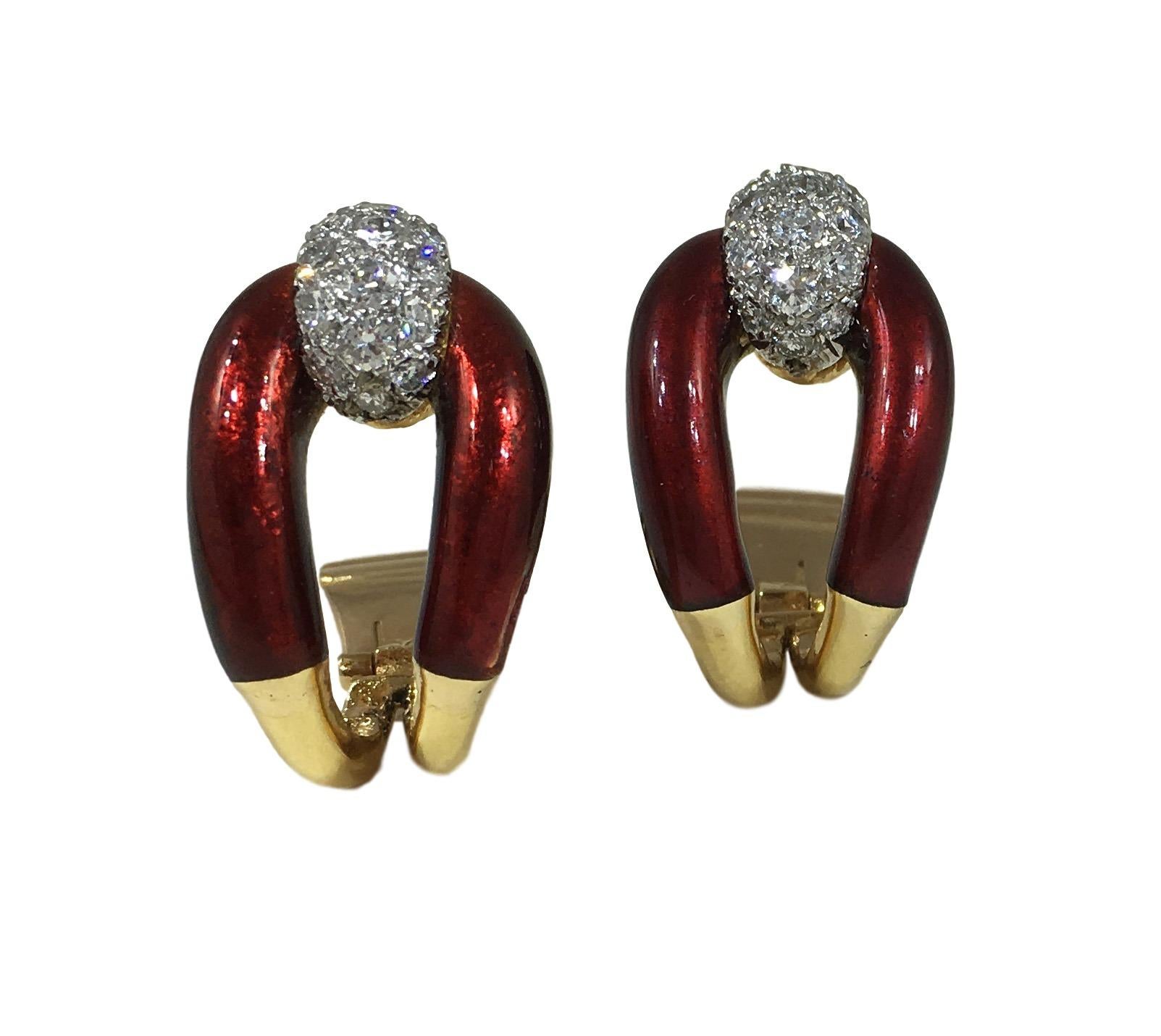 A chic pair of clip earrings in 18 carat gold designed as a buckle, partly enamelled in rich crimson. The bar of each buckle is represented by a diamond bombe finial in white gold pavé-set with 16 round brilliant diamonds with a total approximate