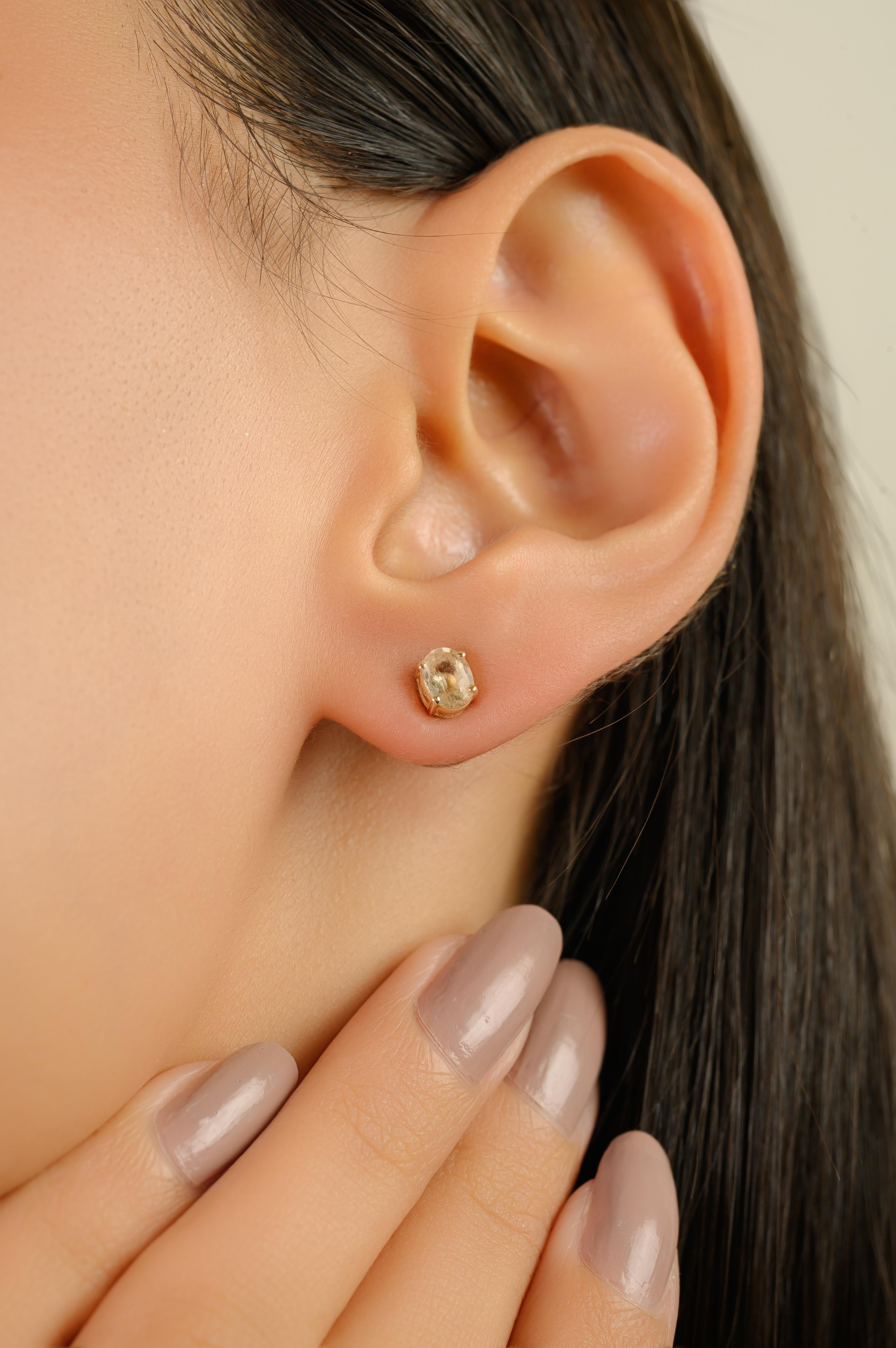 Boucles d'oreilles minimales en or jaune 14 carats, ornées de deux saphirs jaunes de taille ovale d'un poids total de 0,8 carats. Chaque pierre précieuse mesure environ 5 x 4 mm et est gracieusement fixée dans une monture raffinée à quatre griffes.