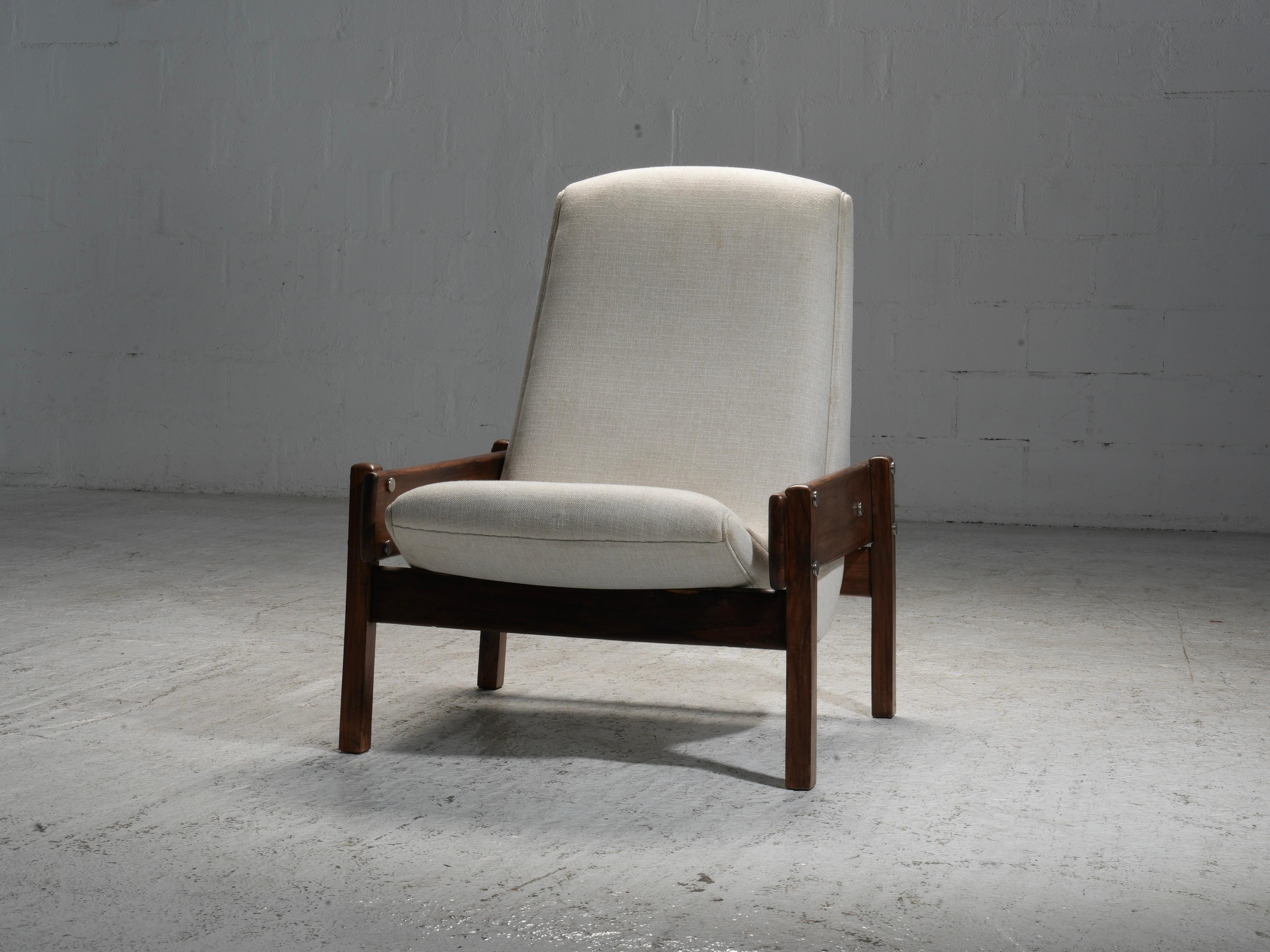 The 'Vronka' chair by Sergio Rodrigues from the 1960s showcases a straightforward, structured design. Its frame is constructed from wood, with broad, flat arms that extend outward from the backrest. The backrest and seat are cushioned, providing a