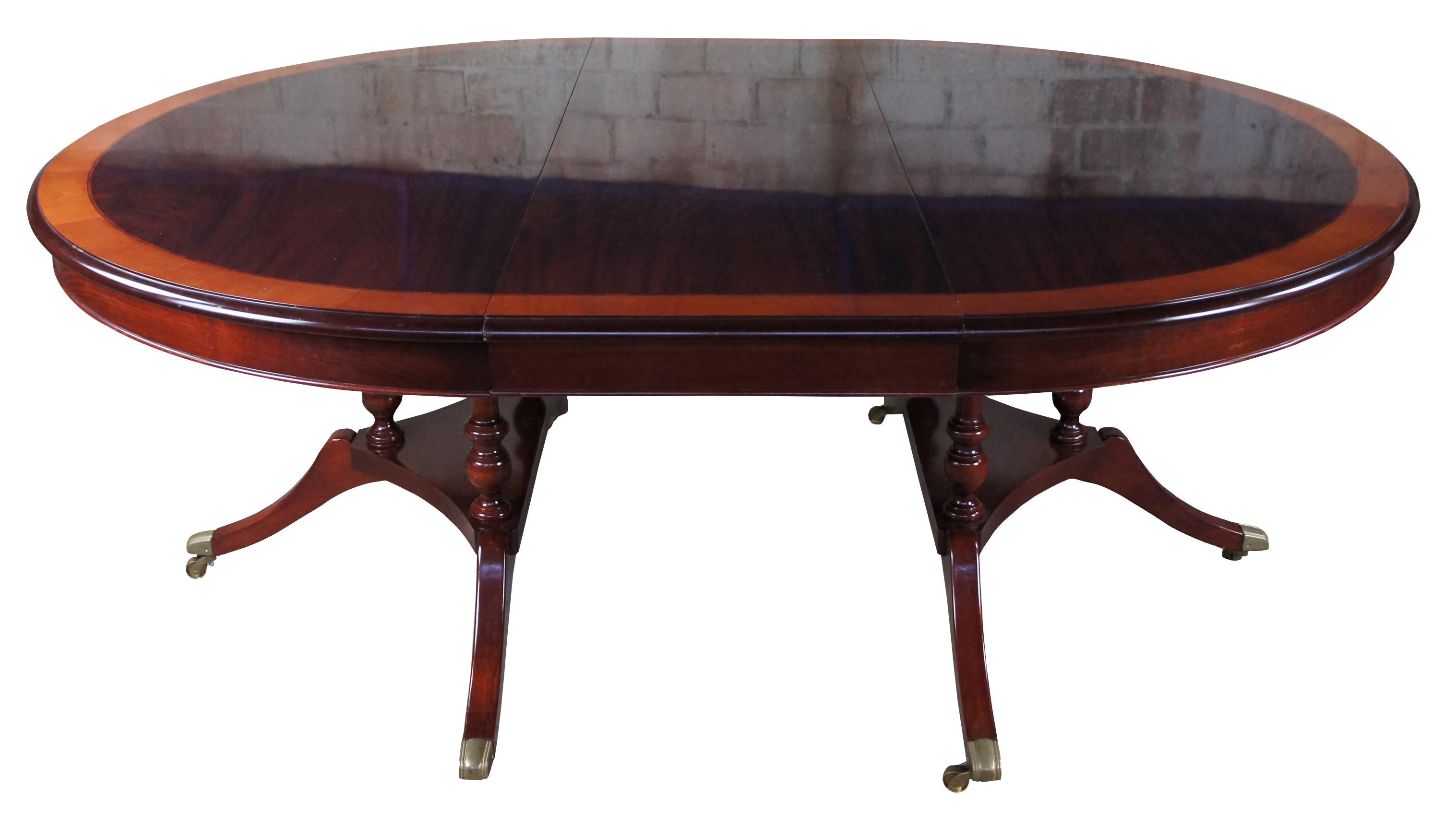 Vintage flame mahogany pedestal table featuring round or oval form with banded top, double pedestal base and swivel castors. Attributed to Ethan Allen's 18th Century Collection.

Two 20