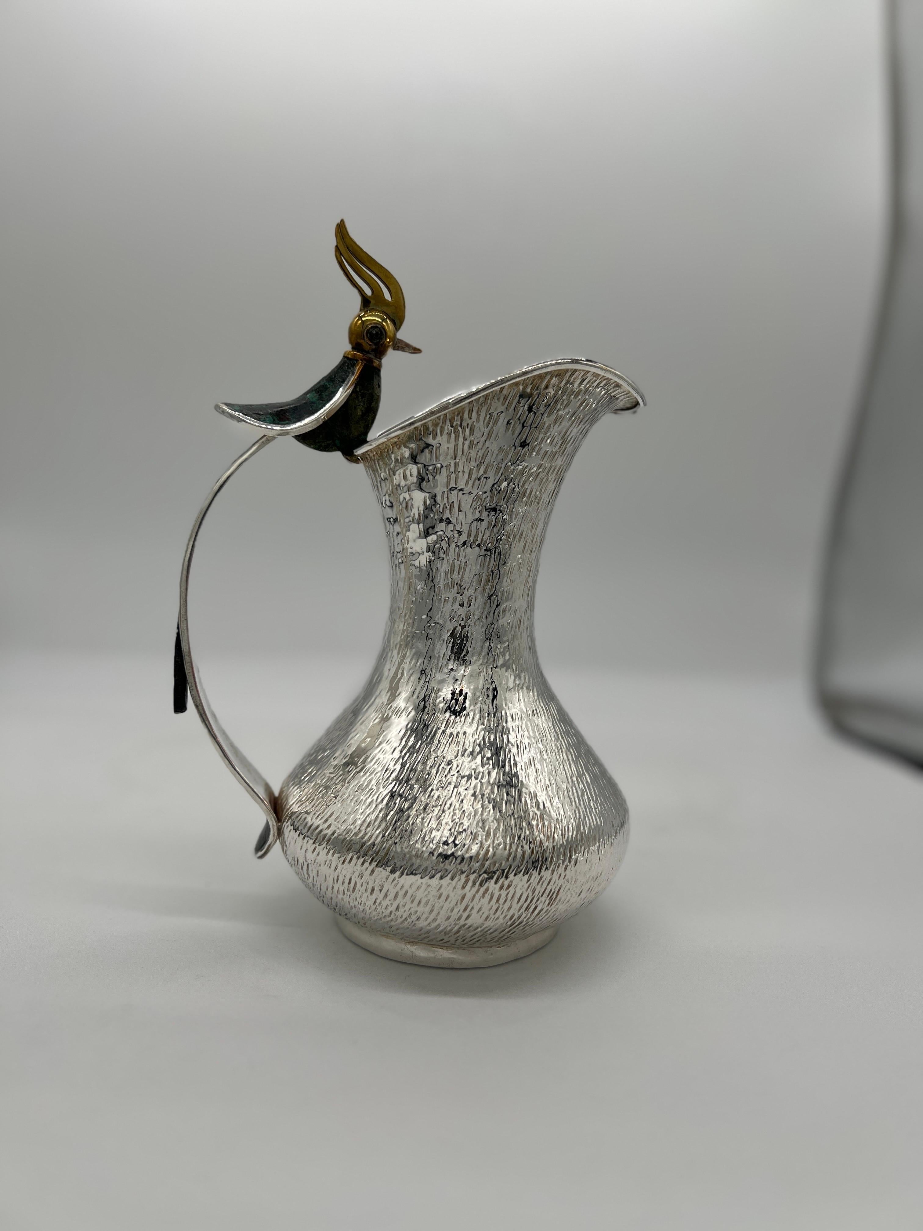 Los Castillo (Mexican, founed 1939), circa 1970. 

A silverplated pitcher with hand hammered and sculpted finish. The pitcher is affixed with a brass hummingbird adorned with lapis and malachite veneer, the tail of the bird forms the pitcher's