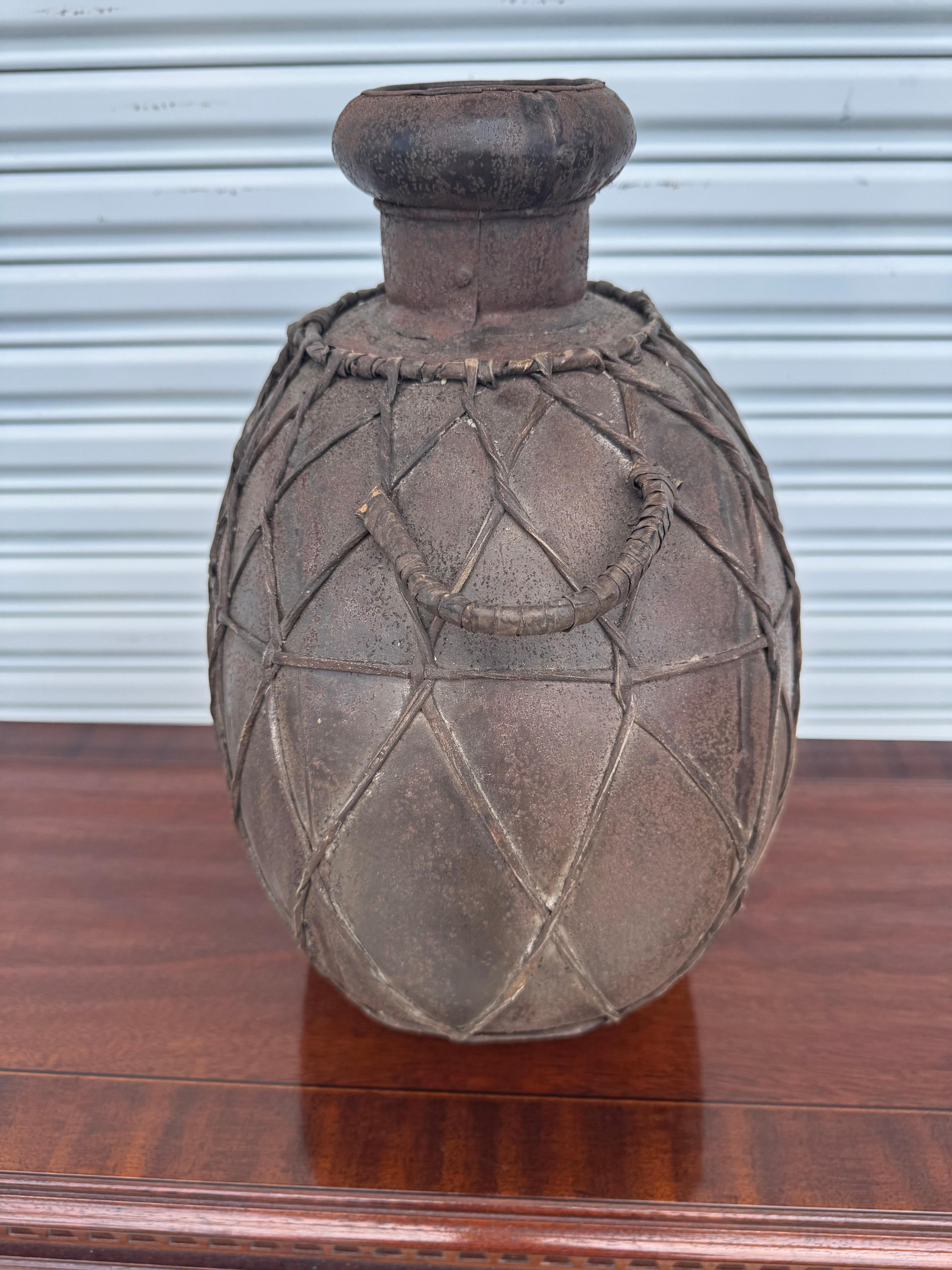 Cette authentique cruche italienne vintage, dotée d'un corps en métal fabriqué à la main et enveloppé d'un riche cuir marron, est munie d'une double poignée ornée pour faciliter le transport. La finition rustique antique et l'artisanat italien font