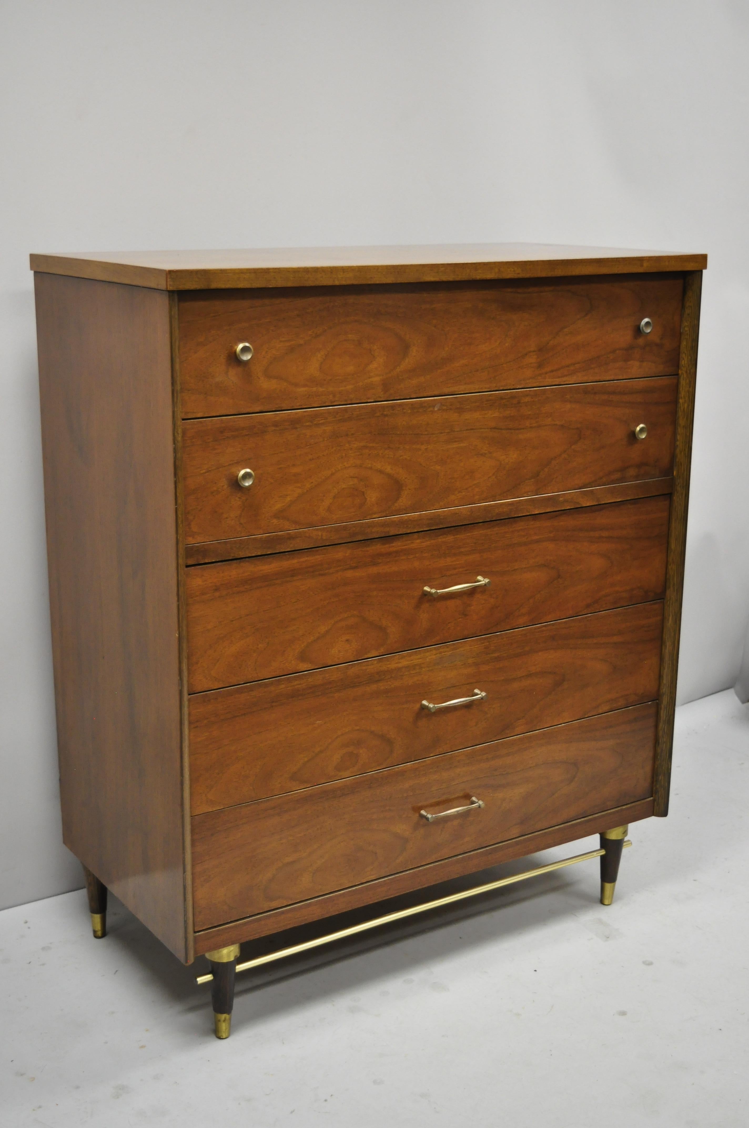 Vintage Mid-Century Modern walnut tall chest dresser by Bassett with brass stretcher base. Item features brass stretcher base, beautiful wood grain, 5 dovetailed drawers, tapered legs, clean modernist lines, great style and form, circa mid-20th