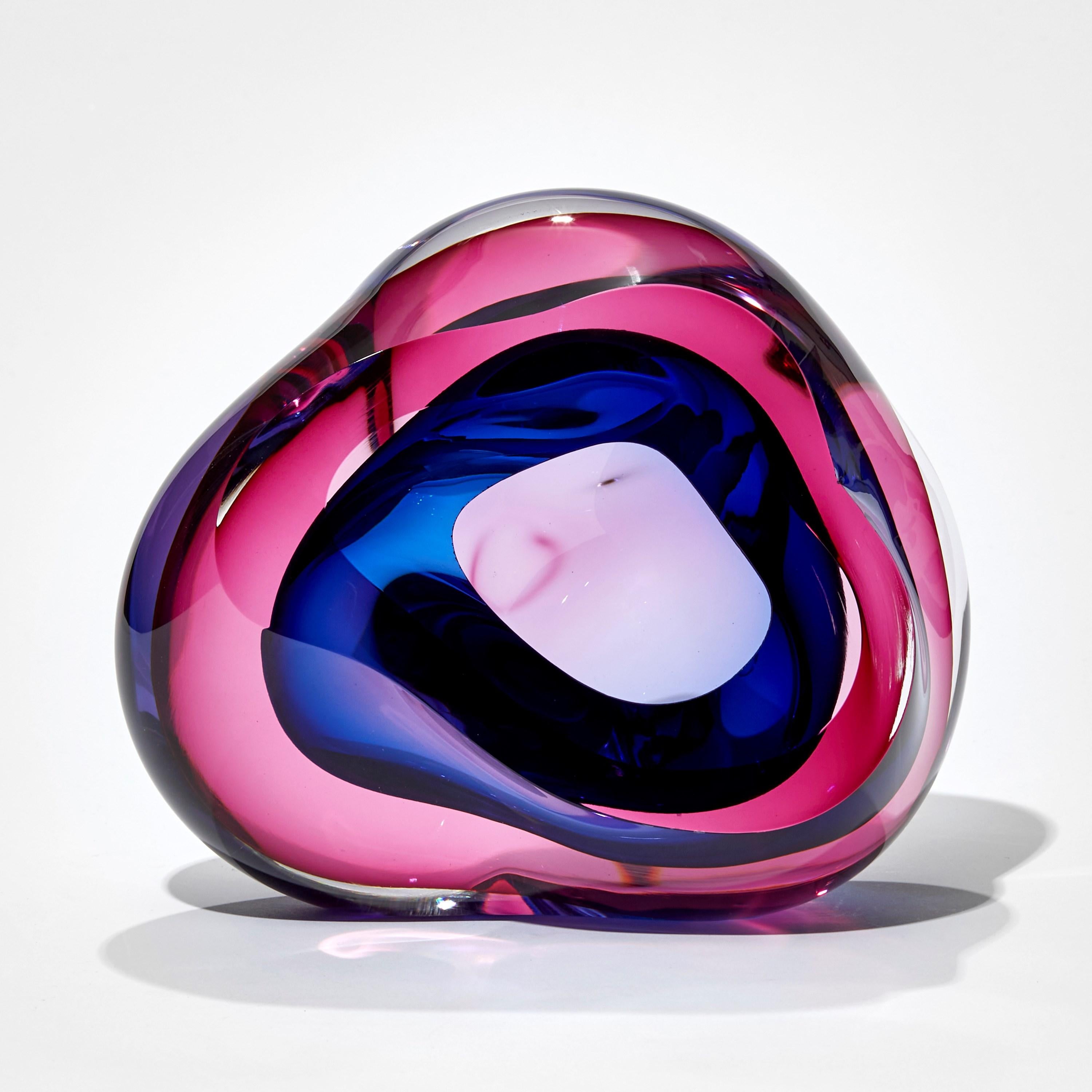 Vug in Fuchsia and blue is a unique hand-blown sculpture by the British artist Samantha Donaldson. Created by layers of colored glass in bright pink and deep blue, the transparent colors merge and create further hues throughout the piece. An