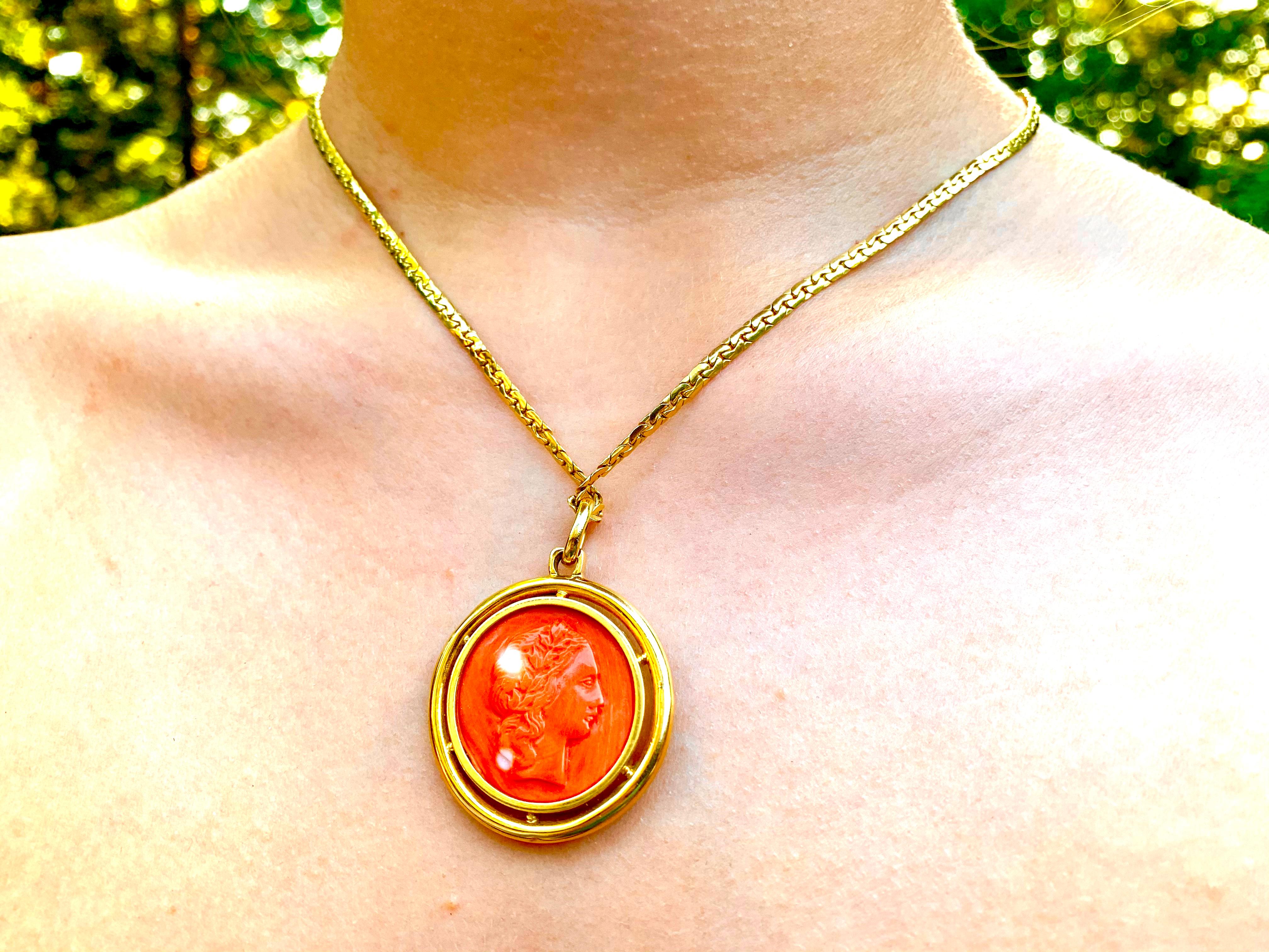 Magnifique médaillon double face en corail rouge naturel sur chaîne en or jaune 18 carats représentant Vénus et Vulcain. 
20ème siècle
Médaillon : 42 mm par 32 mm
Longueur de la chaîne : 450 mm
Depuis des milliers d'années, le corail rouge est