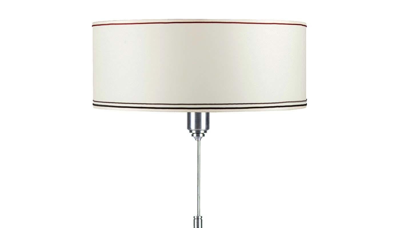 Brimming with contemporary appeal, this refined table lamp will update the aesthetic of any interior as it lends ambient light from the delicate silk drum shade in ivory accented with gray and red stripes along the top and bottom rims. The steel