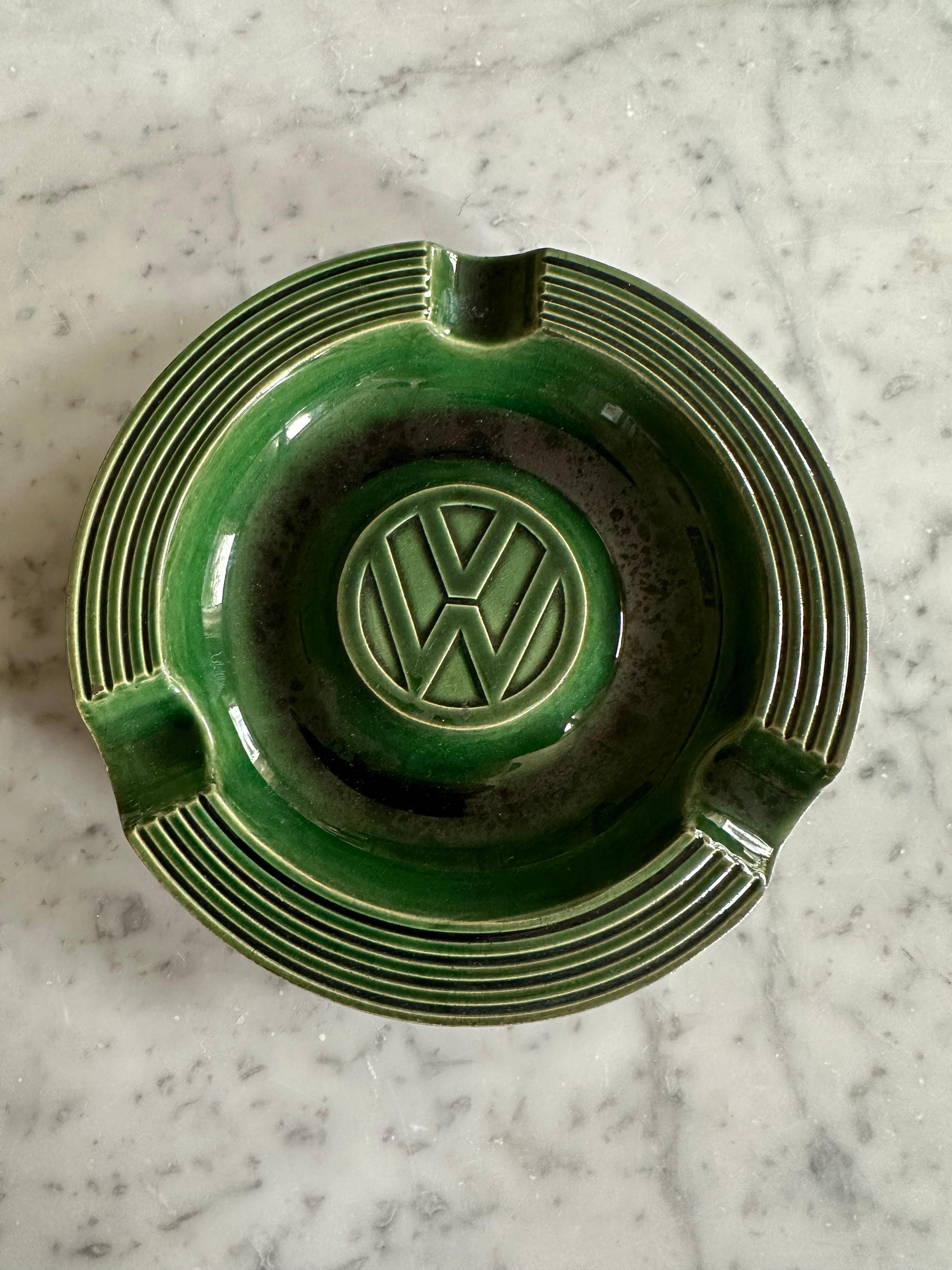 This rare and original Volkswagen (VW) ashtray is a beautiful piece of mid-century design, dating back to the 1950s or 1960s. Crafted from high-quality ceramic, it boasts a sleek, dark green glossy glaze that enhances its timeless appeal. The