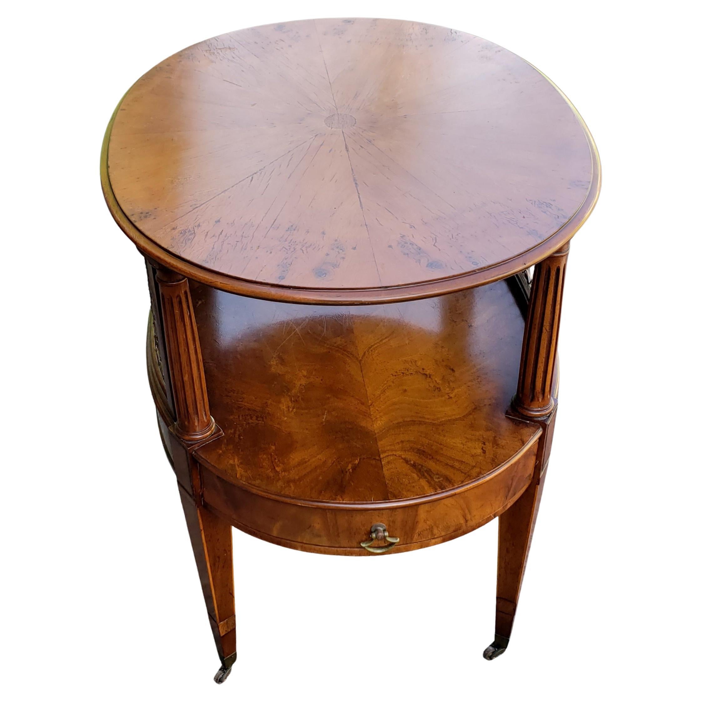 William A. Berkey (American, 1881-1976) for John Widdicomb oval two tiered occasional table, cart table, serving table. Banded mahogany with tapered column supports and wire mesh sides; single lower drawer; on tapered legs with casters. Good vintage