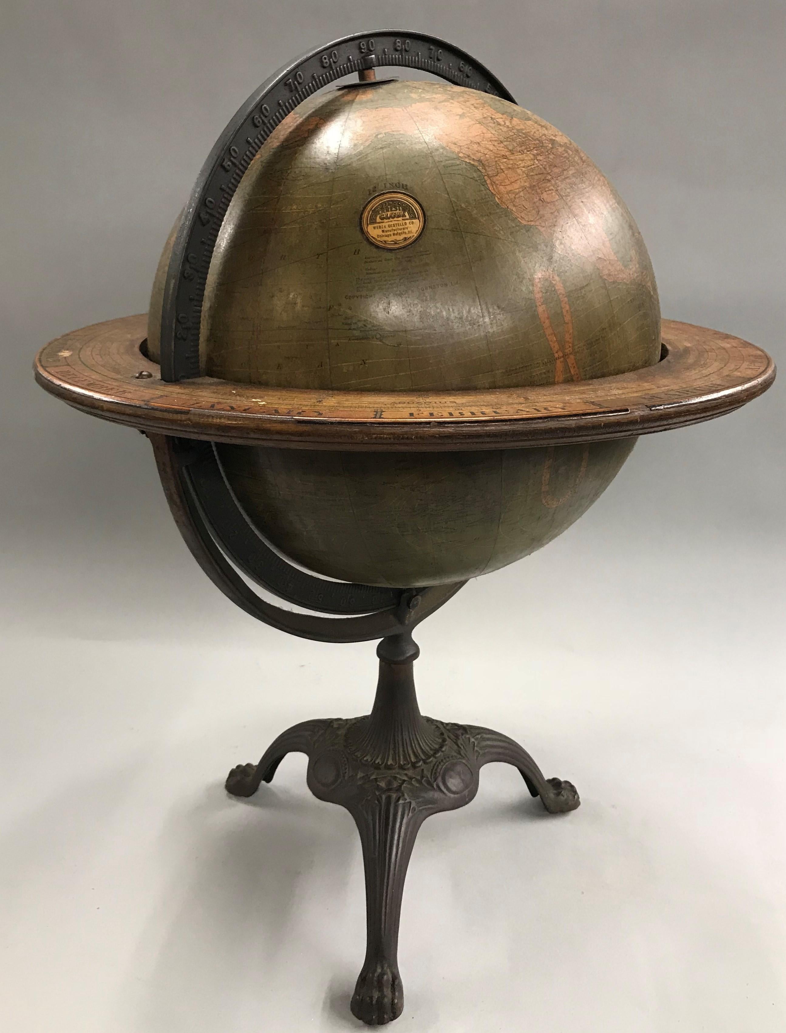 A fine 12 inch terrestrial W. & A.K. Johnston copyright globe by Weber Costello of Chicago Heights, IL with embossed graduated cast iron Meridian ring, wooden horizon ring depicting months and zodiac signs, all supported by a tripod cast stand with
