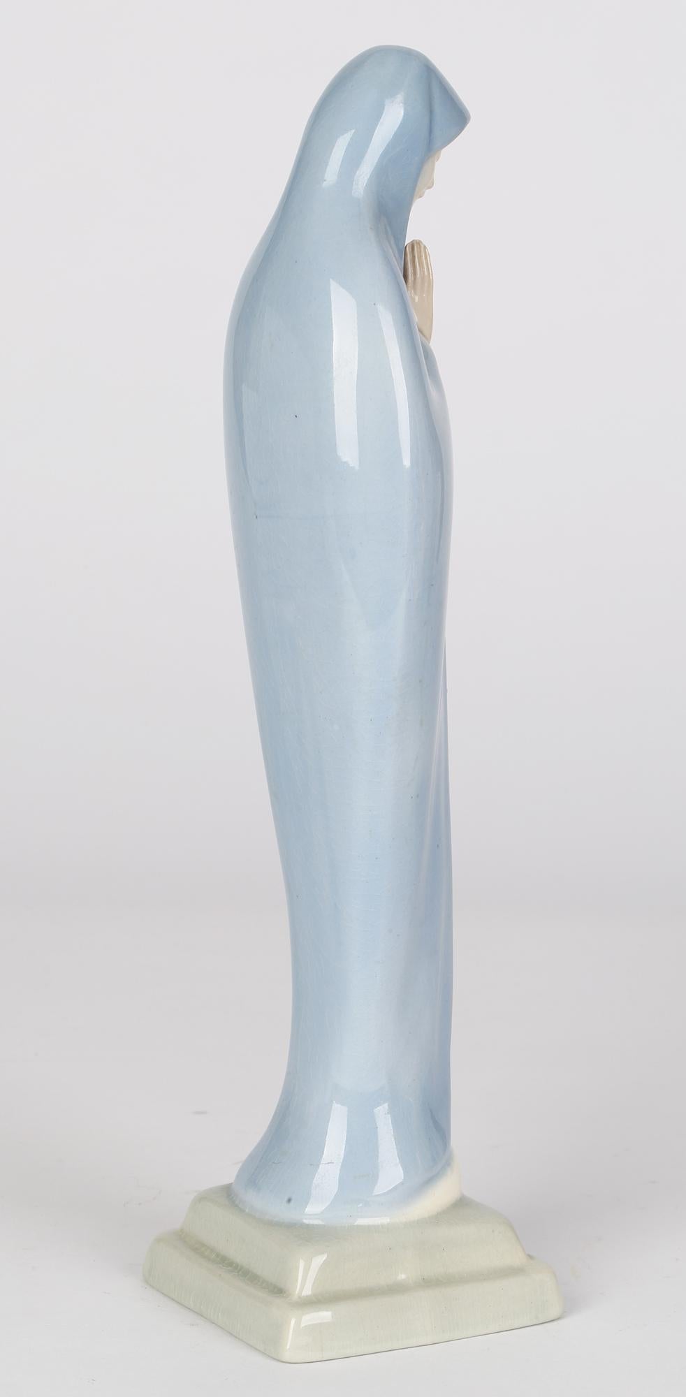 A fine mid-century, late art deco, painted ceramic figure of the Virgin Mary by W R Midwinter, Burslem and dating from around 1950. The figure stands raised on a dome mounted on a stepped square base and portrays Mary wearing a full length and