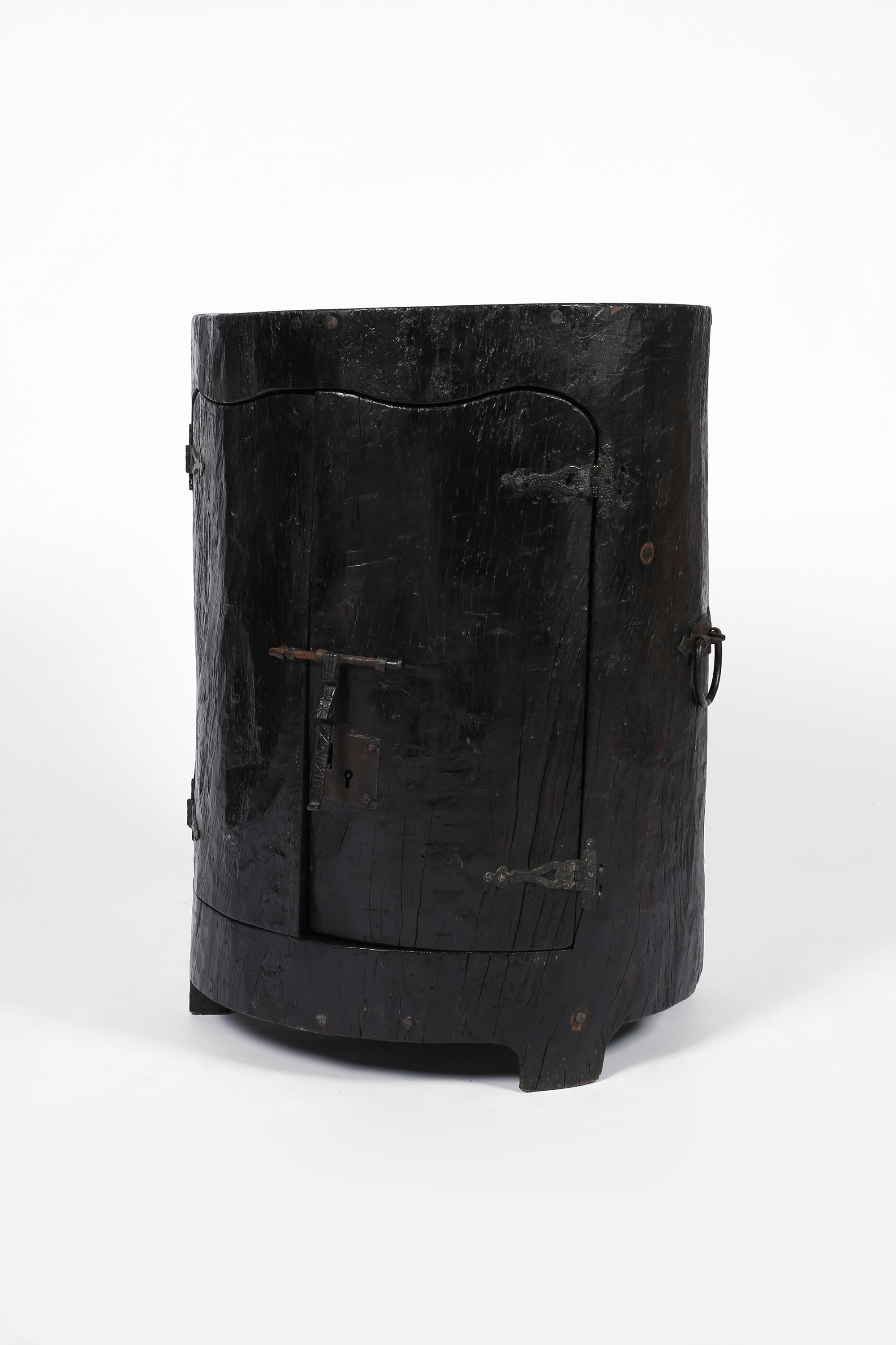 A low dug-out folk-art cupboard formed from a hollowed out and ebonised chestnut trunk. Featuring decorative forged iron hardware, the two shaped doors open to reveal a single shelf within. Portuguese, early-mid 20th century.