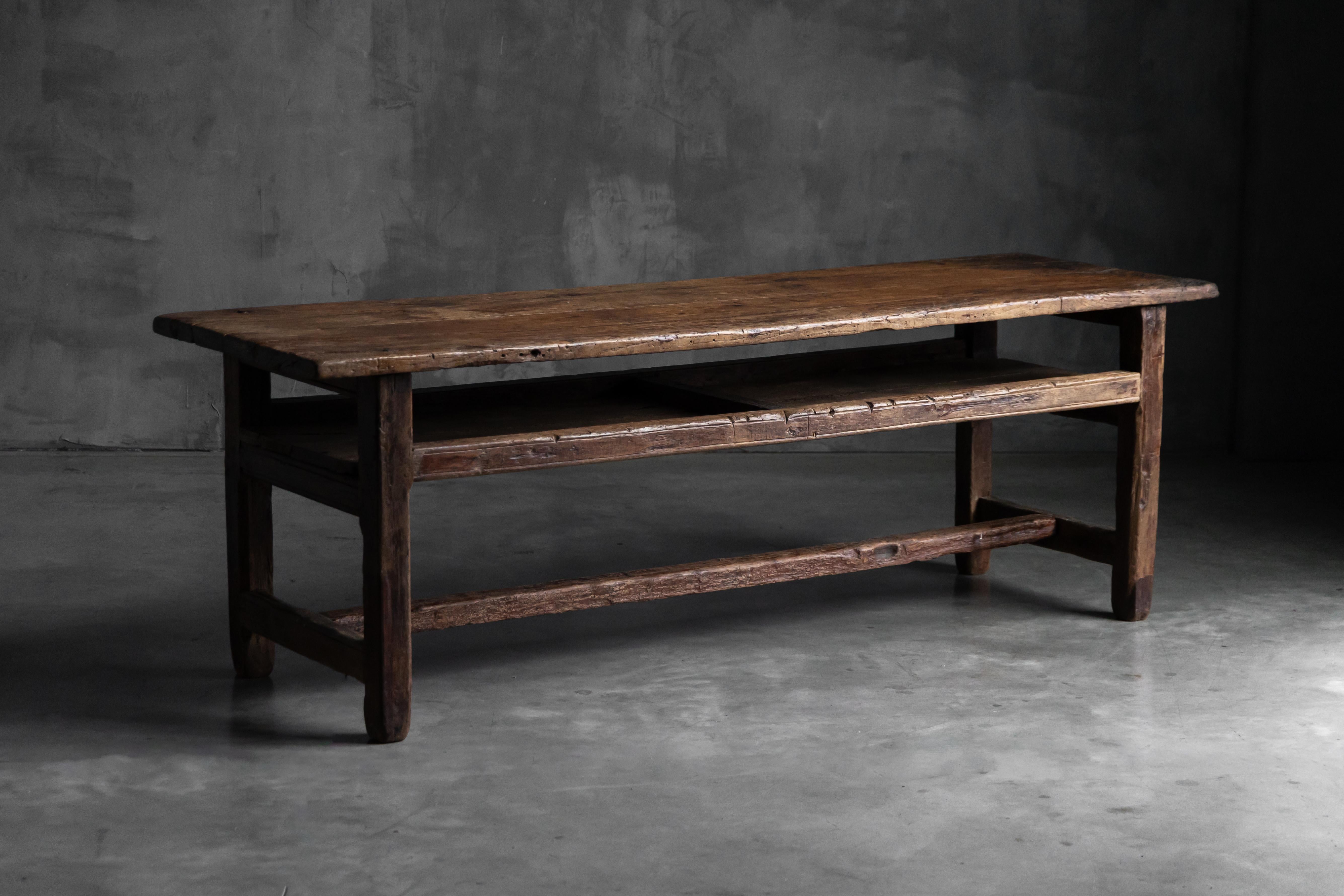 Cette table du XIXe siècle, fabriquée en orme massif, incarne l'essence même du wabi-sabi avec ses bords irréguliers, sa patine profonde et sa surface usée par le temps. Conçue avec une généreuse étagère ouverte sous le plateau, elle fonctionne