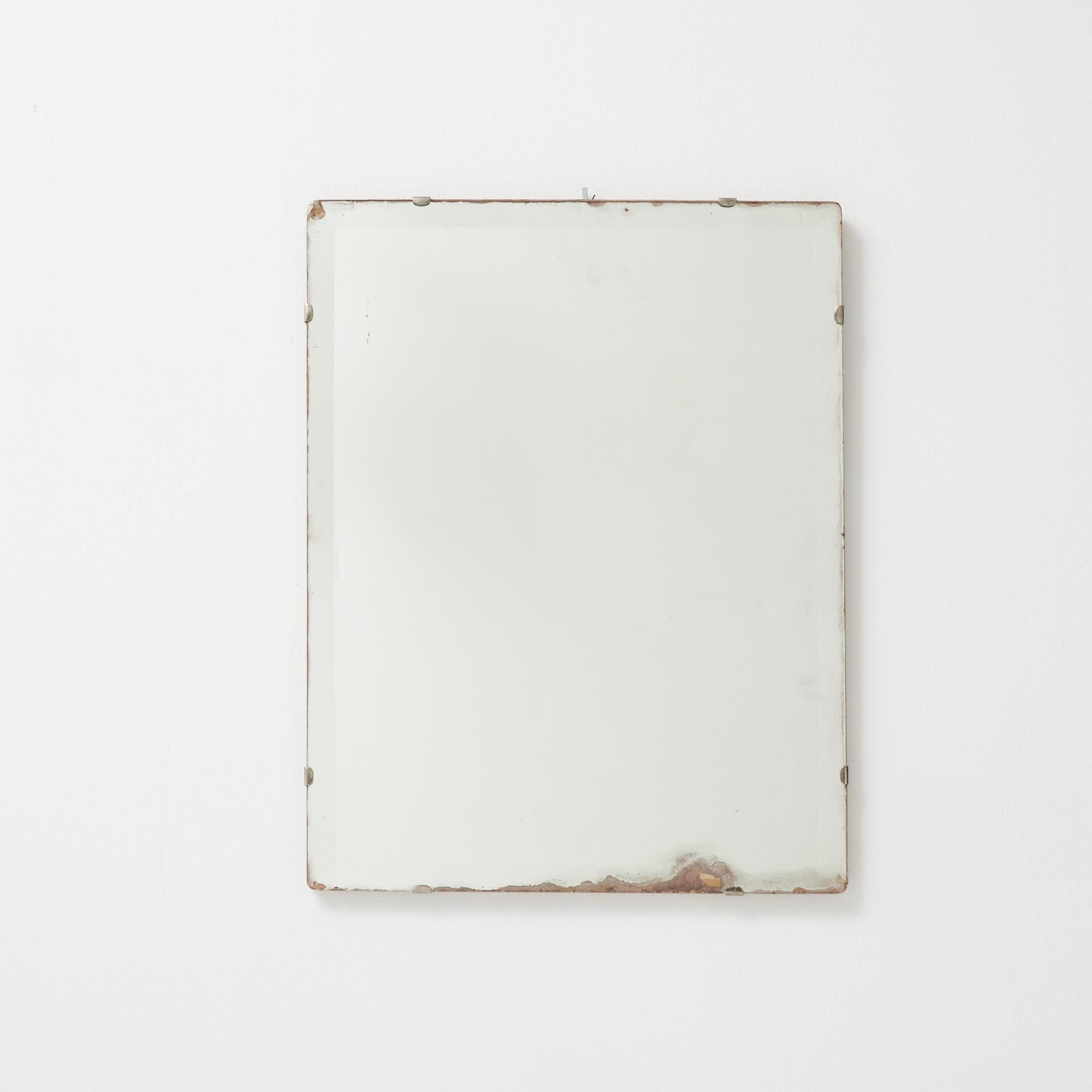 A bold and authentic French industrial mirror from the 1940s, this rectangular wall piece embodies raw materiality and quiet resilience. Stripped of ornament, the mirror plate is exposed and mounted directly with small metal clips, revealing edge