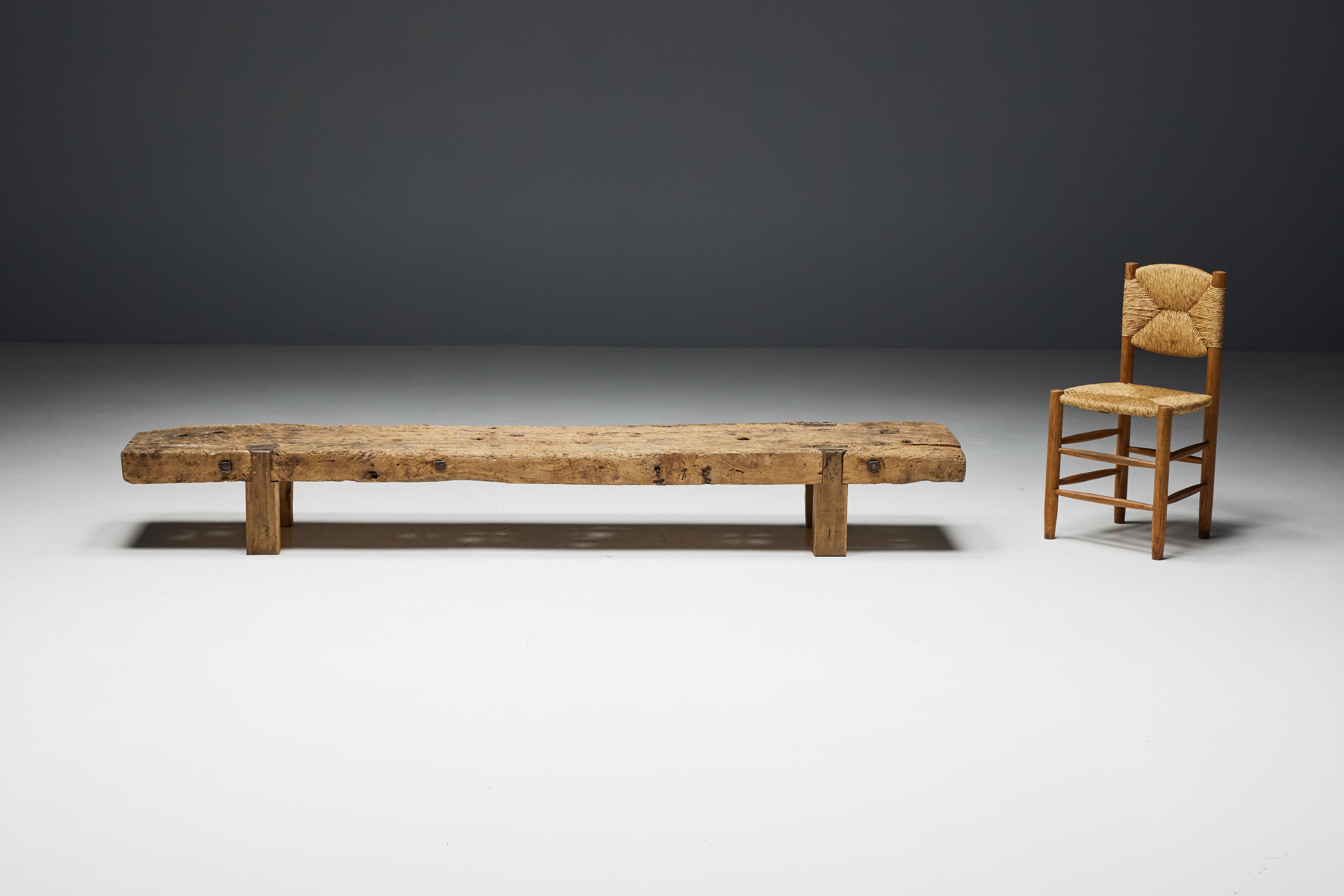 Primitive rustic bench or coffee table made of sturdy wood with a weathered finish. The natural wear of the wood over the years has created a unique, rustic look that adds character and depth to the bench. The generous size of this bench also allows