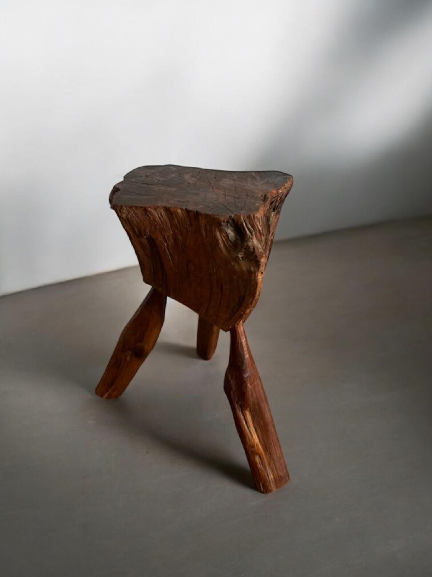 This expressive three-legged stool is a raw and organic piece, hand-carved from solid natural wood, retaining the irregularities, texture, and form of its original log. The triangular seat and asymmetrical legs showcase the artisan’s minimal