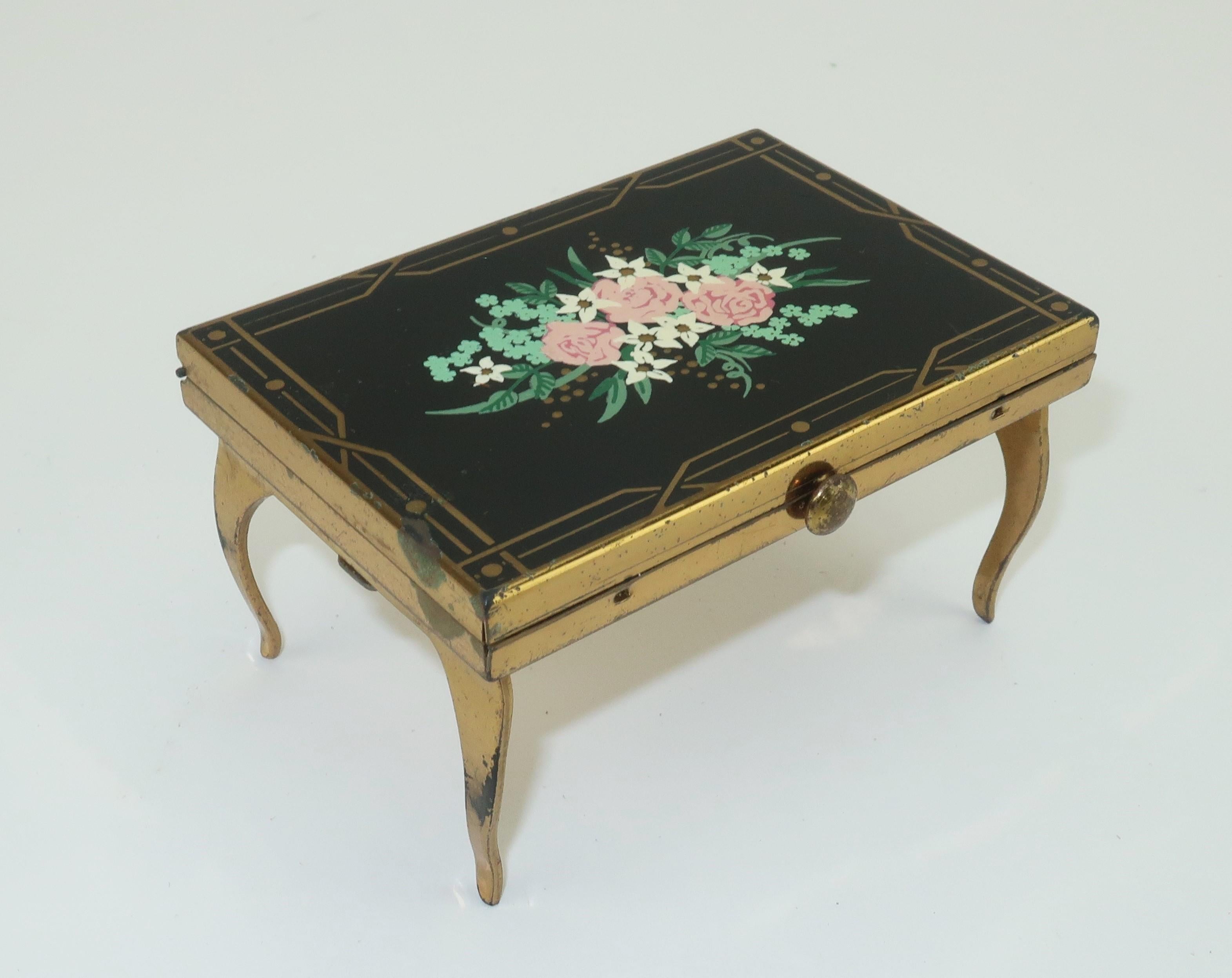 Adorable C.1950 Wadsworth powder compact with a black painted enamel top accented by flowers in shades of pink, white and green. This special compact has a secret … it is actually masquerading as a miniature vanity table! The underside has a