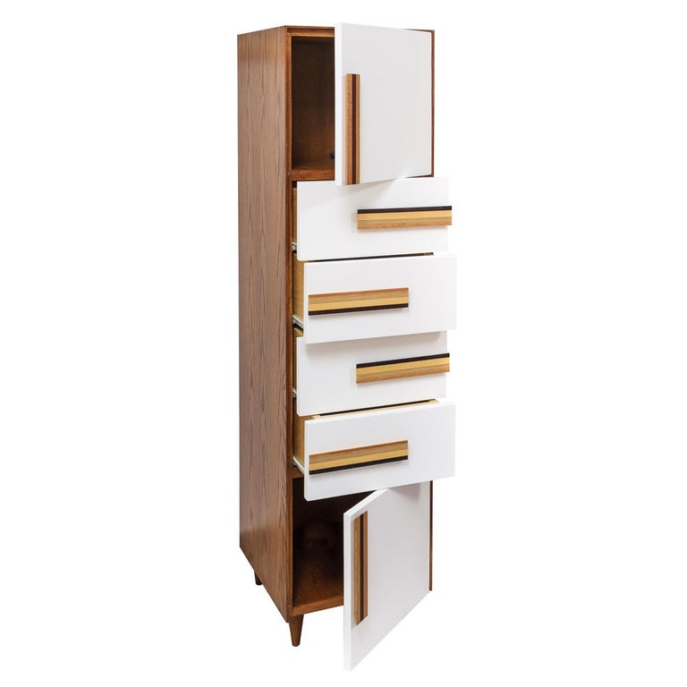 This Postmodern cabinet is distinguished for its deft use of geometries to create an architectural work of art. Crafted entirely of a warm-toned chestnut, the tall silhouette is characterized by a white-finished surface with layered wooden handles,