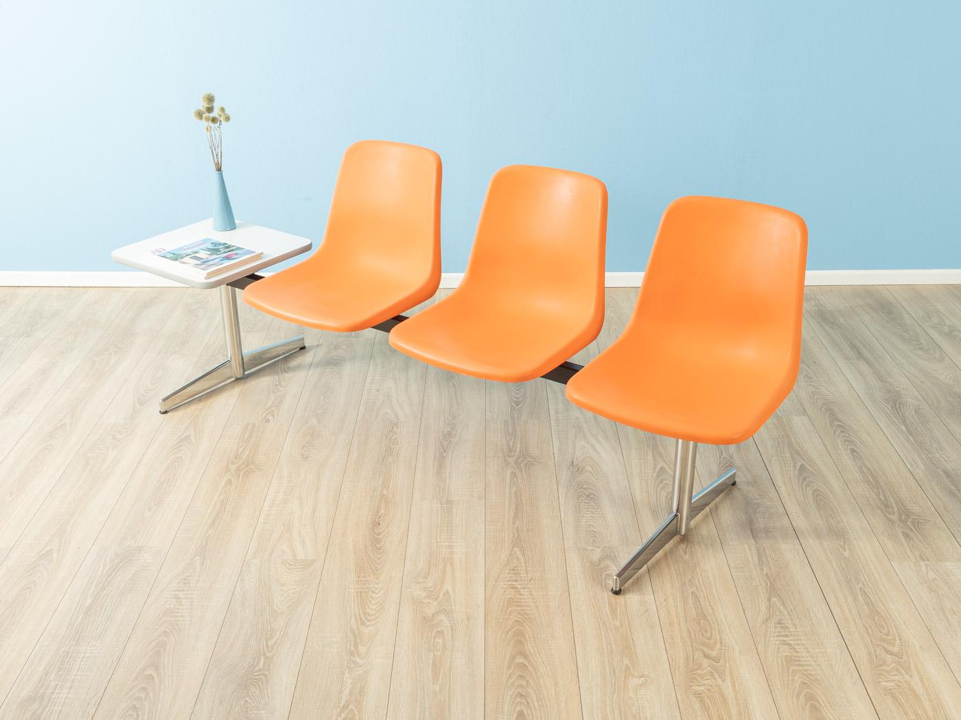 Unique waiting bench from the 1970s, high-quality frame made of steel and stainless steel with three seat shells made of plastic in orange. The table has been coated with white Formica and a fourth seat shell can be mounted instead of the table.