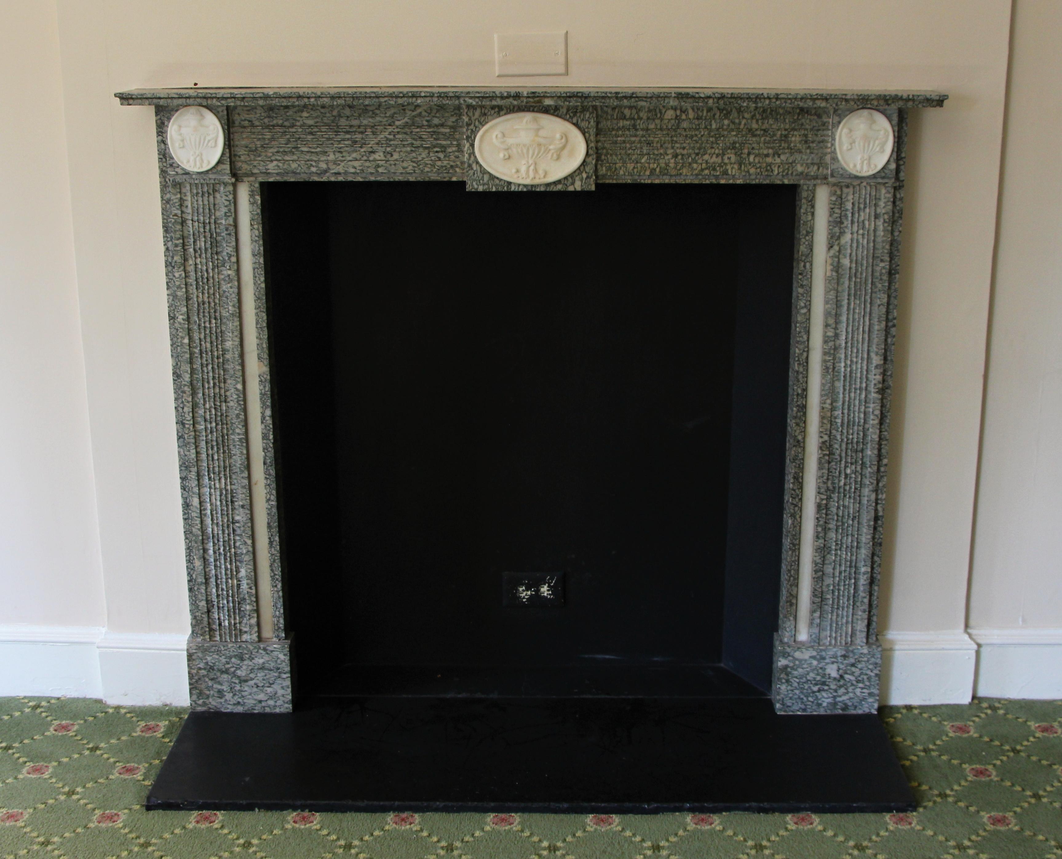 A dainty English Regency-style gray marble mantel from the 19th Century, adorned with delicate white carved urn motifs gracing the top corners and the center of the header. The marble showcases a prominent display of white veining, adding to its